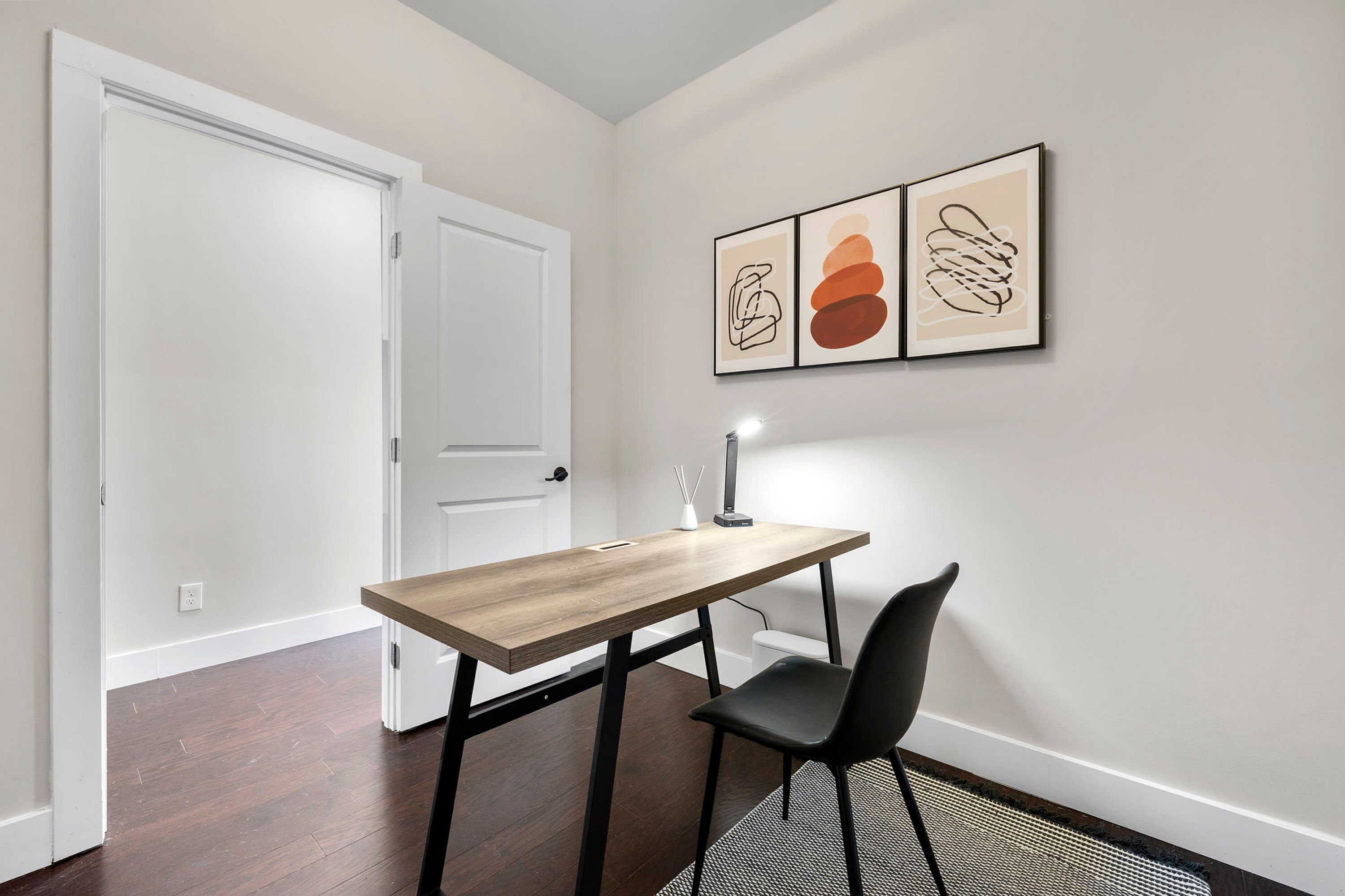 Un petit coin repas avec une table en bois et une chaise noire, une porte blanche et une œuvre d’art abstraite au mur.