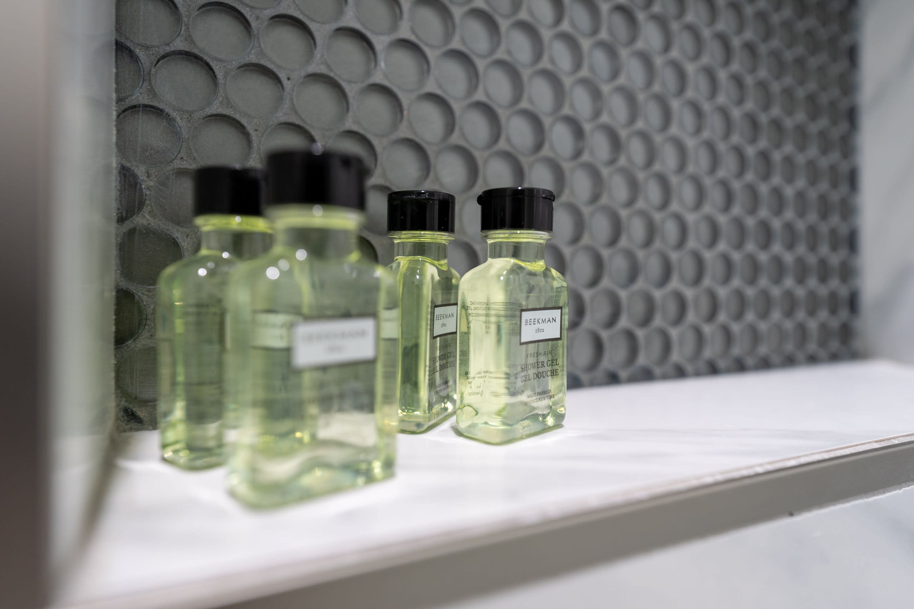 Tres botellas de gel de ducha sobre una repisa frente a una pared con textura.