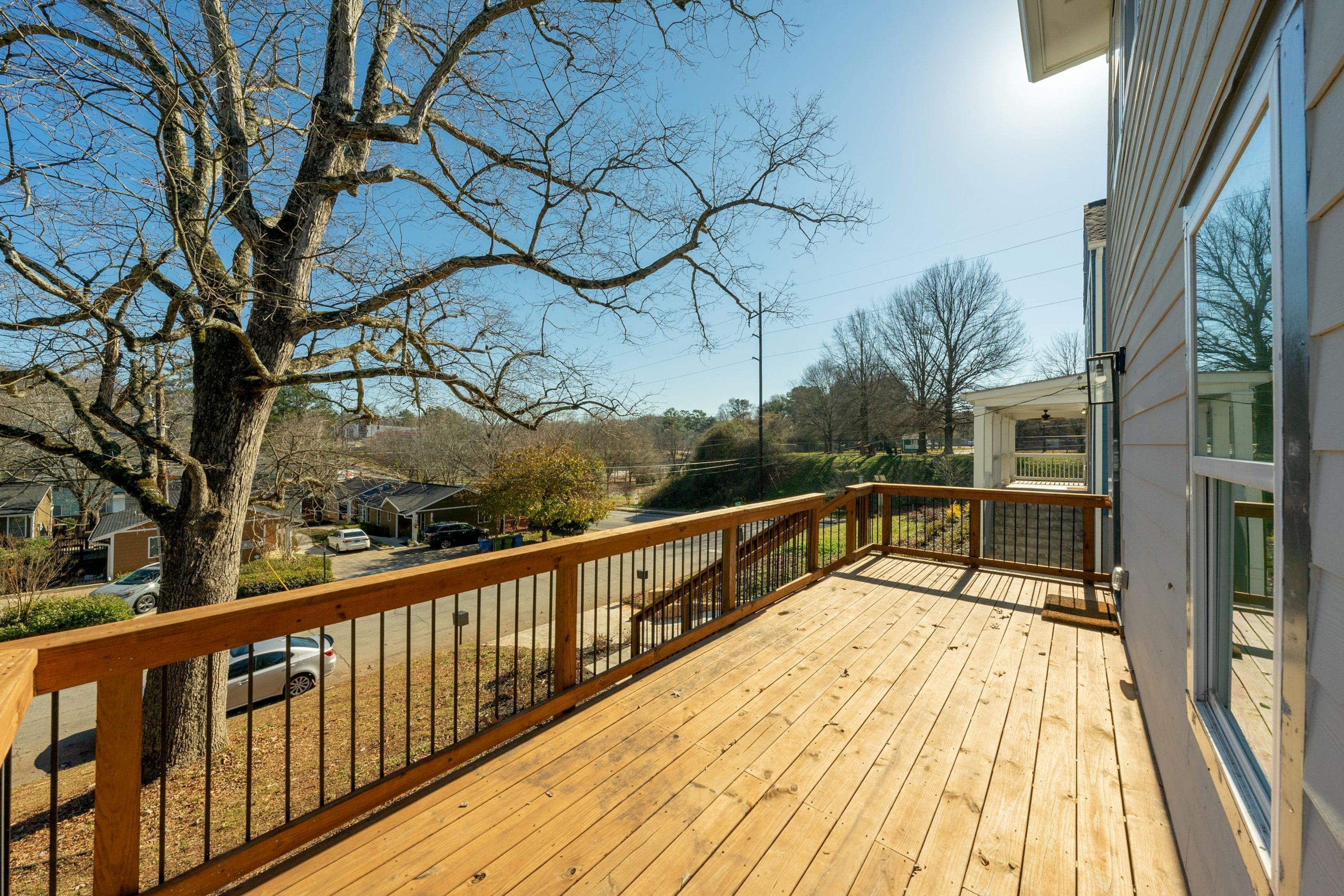 A wooden deck with a railing, overlooking a residential area with houses and a street.