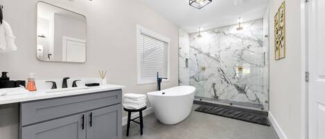 Une salle de bain moderne avec un grand miroir, deux vasques, une baignoire sur pieds et des murs en marbre.
