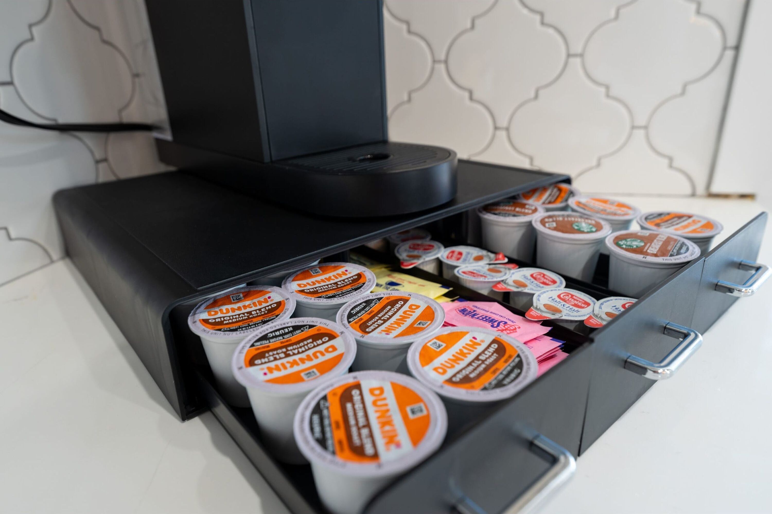 Une machine à café dotée d’un tiroir contenant différentes tasses de la marque Dunkin’ Donuts.
