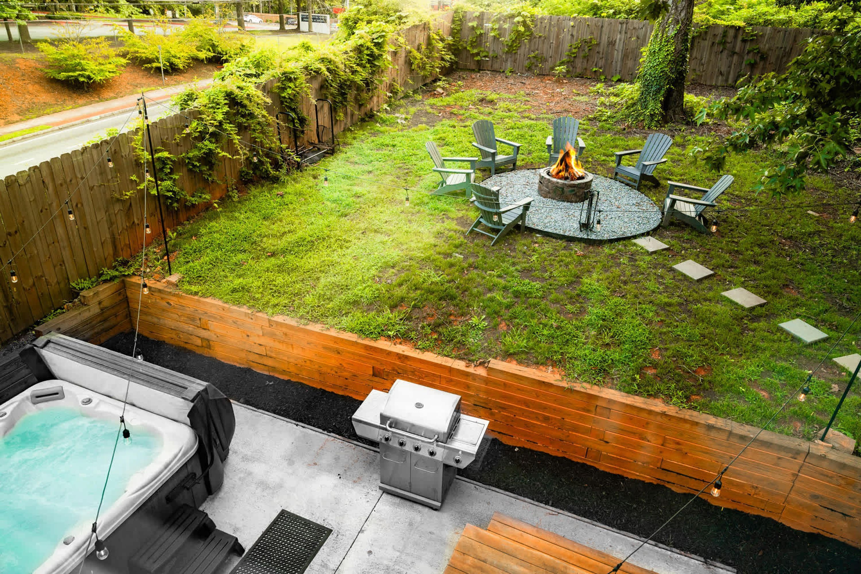 A backyard with a hot tub, a grill, and a fire pit surrounded by chairs.