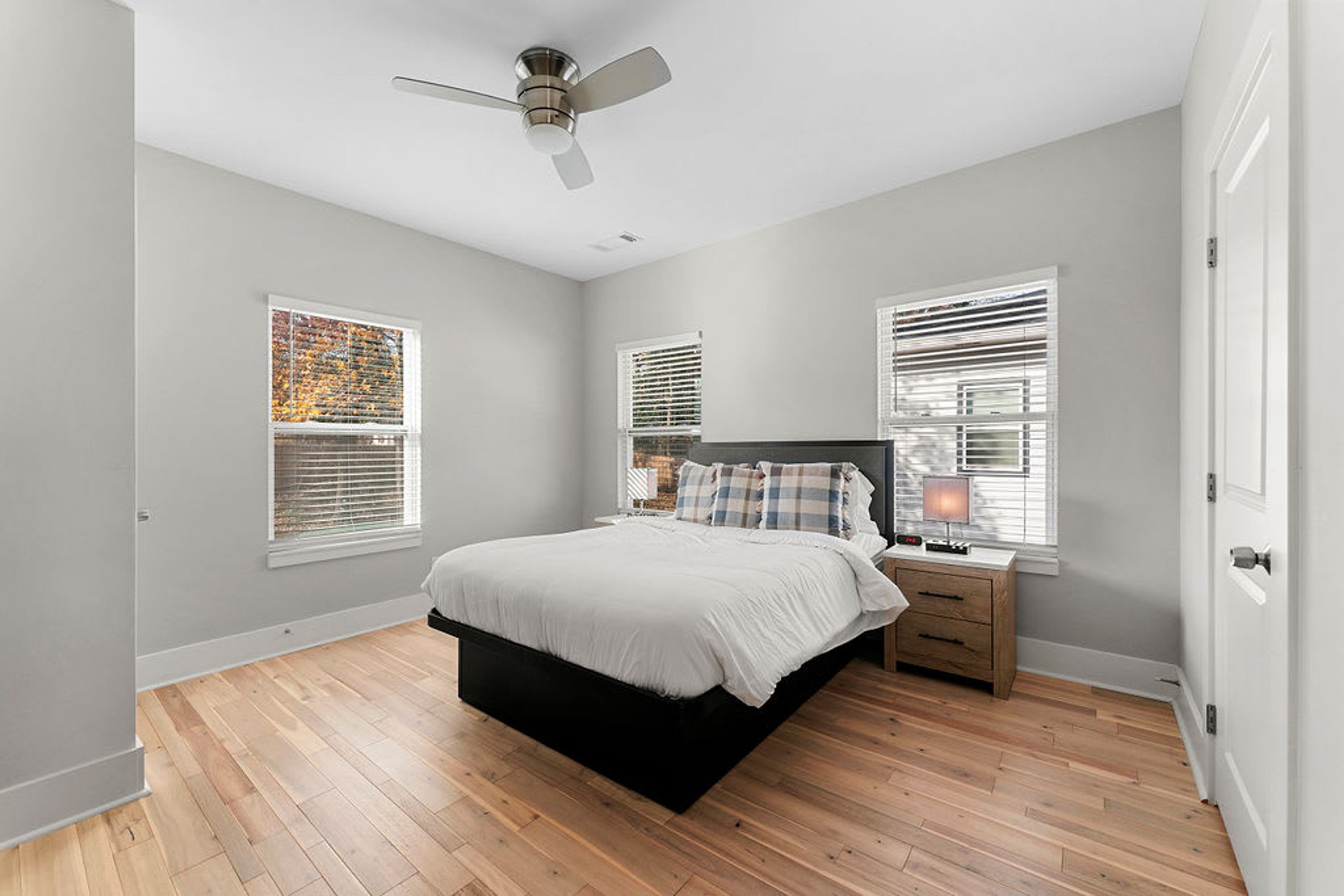A bedroom with a bed, bedside tables, a ceiling fan, and windows with blinds.