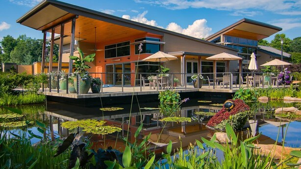 A modern building with a covered patio area, a pond with lily pads, and outdoor seating with umbrellas. - Private Resort - Lake Lanier Paradise (Gainesville)