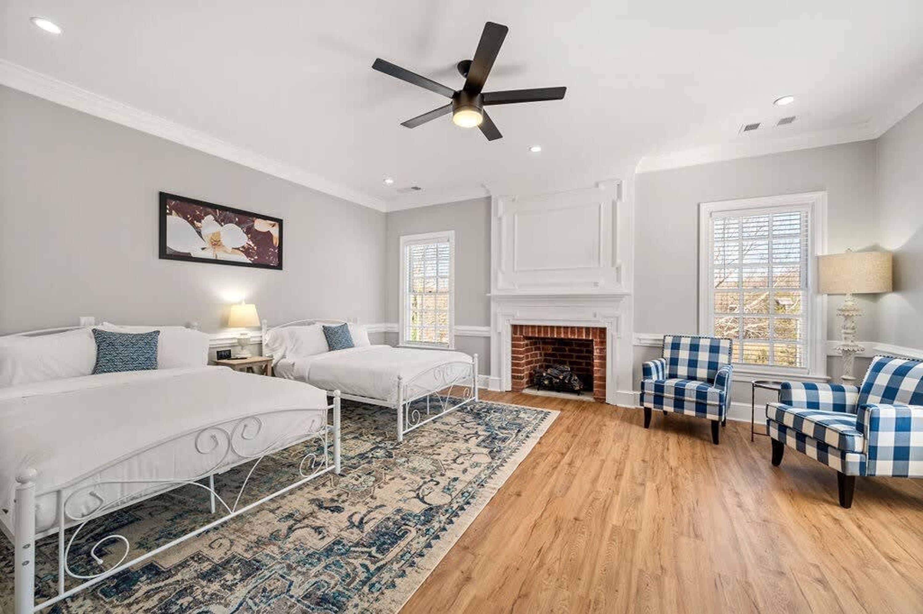 Une chambre avec deux lits, une cheminée, un ventilateur de plafond et une vue sur l’extérieur par une fenêtre.