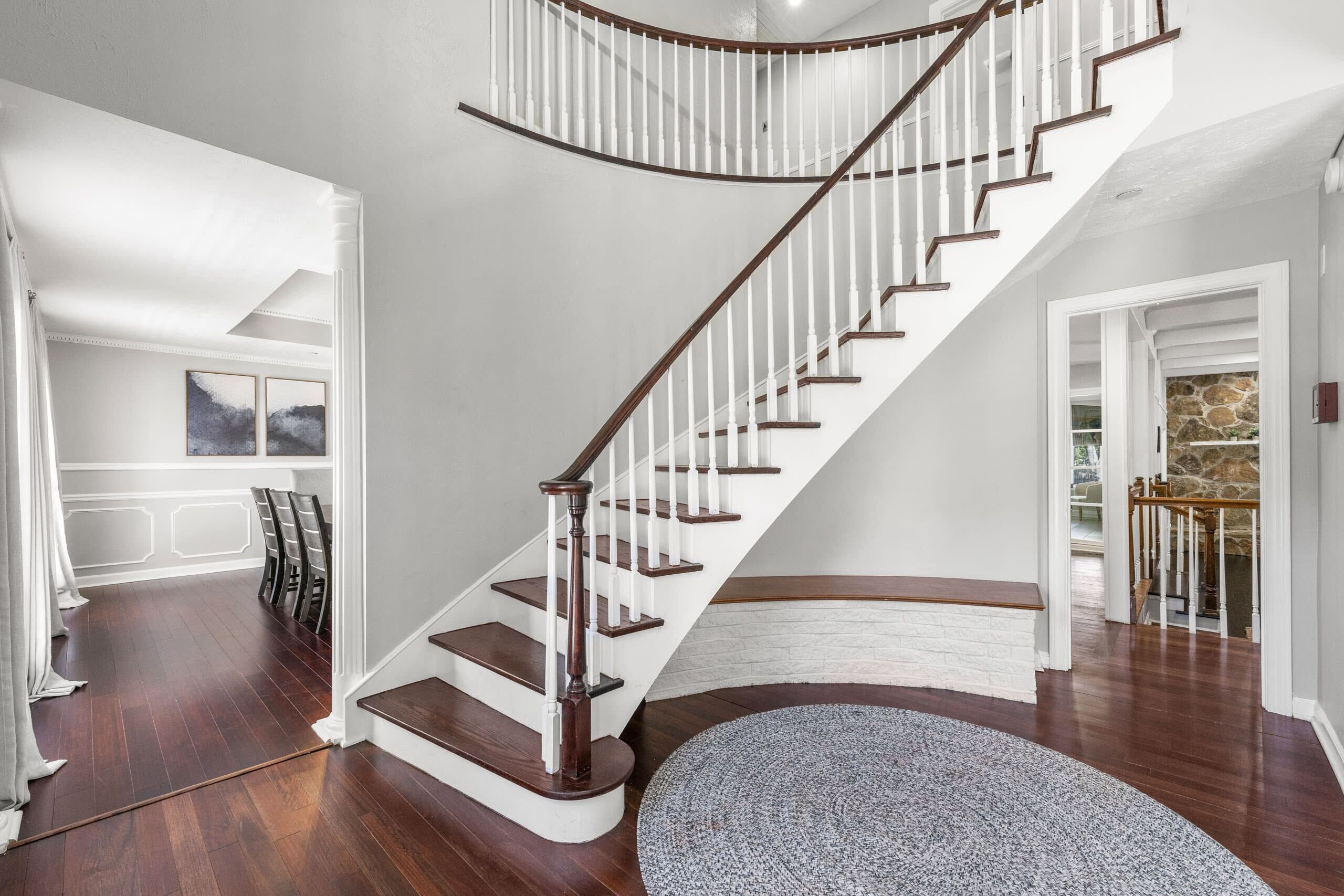 A spacious living room with a curved staircase, hardwood flooring, and a round rug.