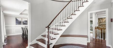 A spacious living room with a curved staircase, hardwood flooring, and a round rug.