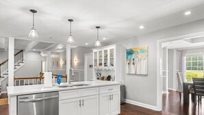A modern kitchen with white cabinets, stainless steel dishwasher, pendant lighting, and a large island. - Mansion With Private Pool Bsktball Tennis Courts (Fayetteville)