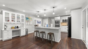 A modern kitchen with white cabinetry, a central island with stools, stainless steel appliances, and recessed ceiling lighting. - Mansion With Private Pool Bsktball Tennis Courts (Fayetteville)