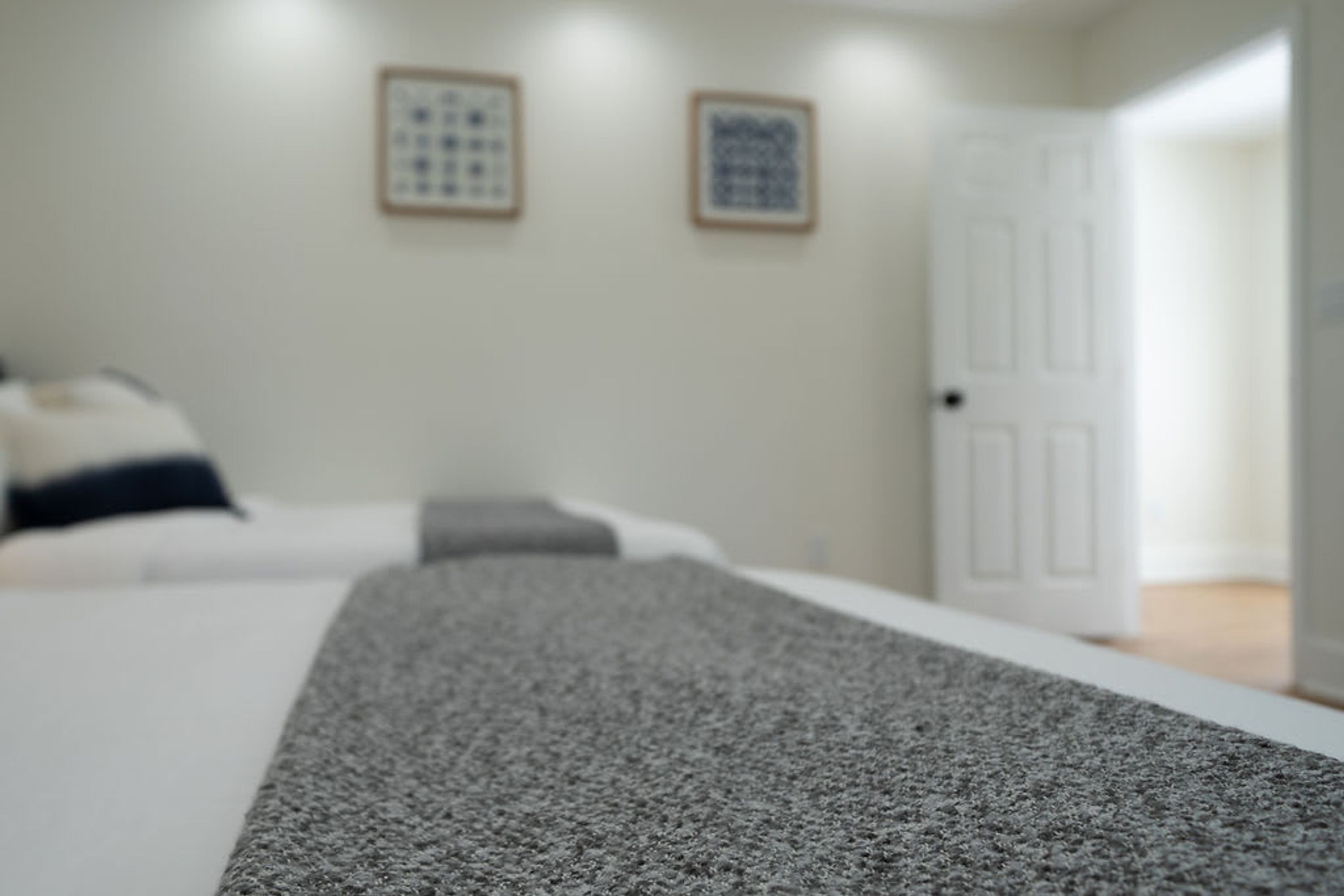 A bedroom with a bed, a gray throw blanket, and two framed pictures on the wall.