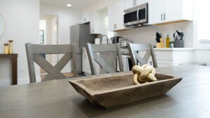 A modern kitchen with white cabinets, a microwave, and a dining area with a wooden table and chairs. - Beautifully Modern Cottage in Historic Norcross (Norcross)