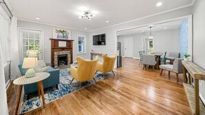 Ein geräumiges Wohnzimmer mit Holzdielen, Kamin, Essbereich und einer Küche im Hintergrund.