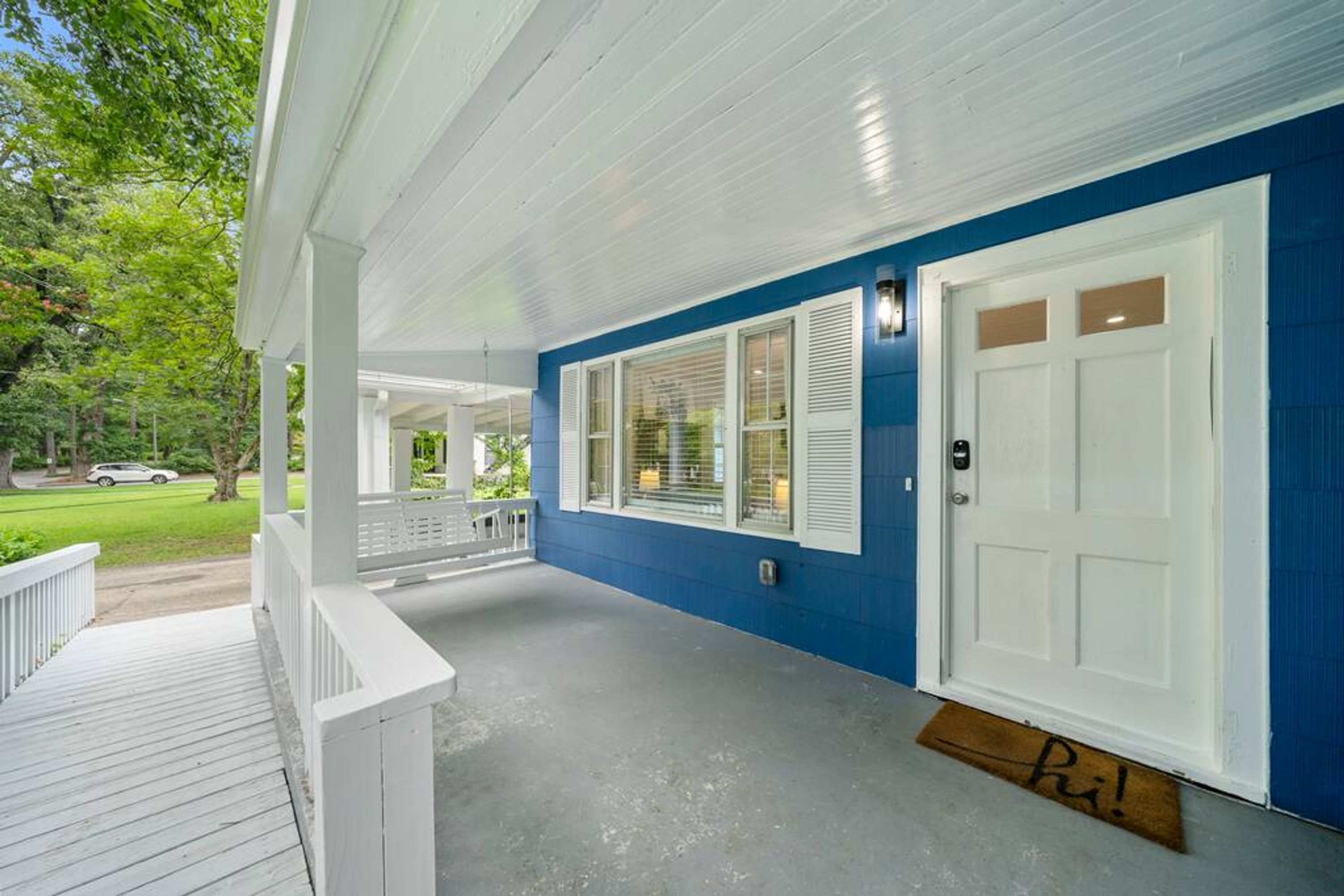 A covered porch with a white railing, a blue exterior wall, and a white door with a doormat.