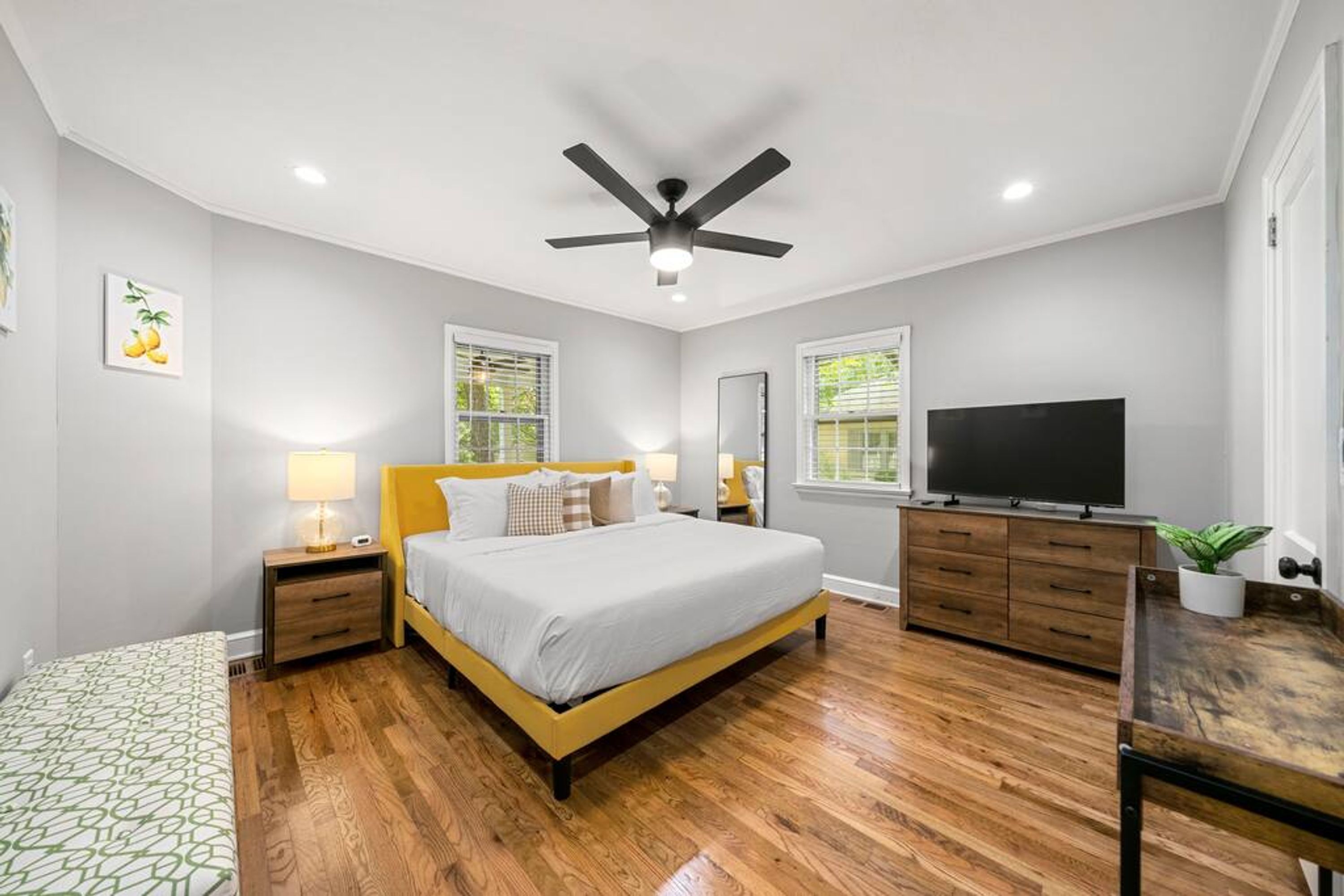 Une chambre à coucher avec un lit, une télévision, un ventilateur de plafond et un plancher en bois.