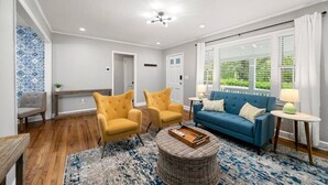 Ein Wohnzimmer mit einem blauen Sofa, zwei gelben Sesseln, einem runden Korbtisch und Holzböden.