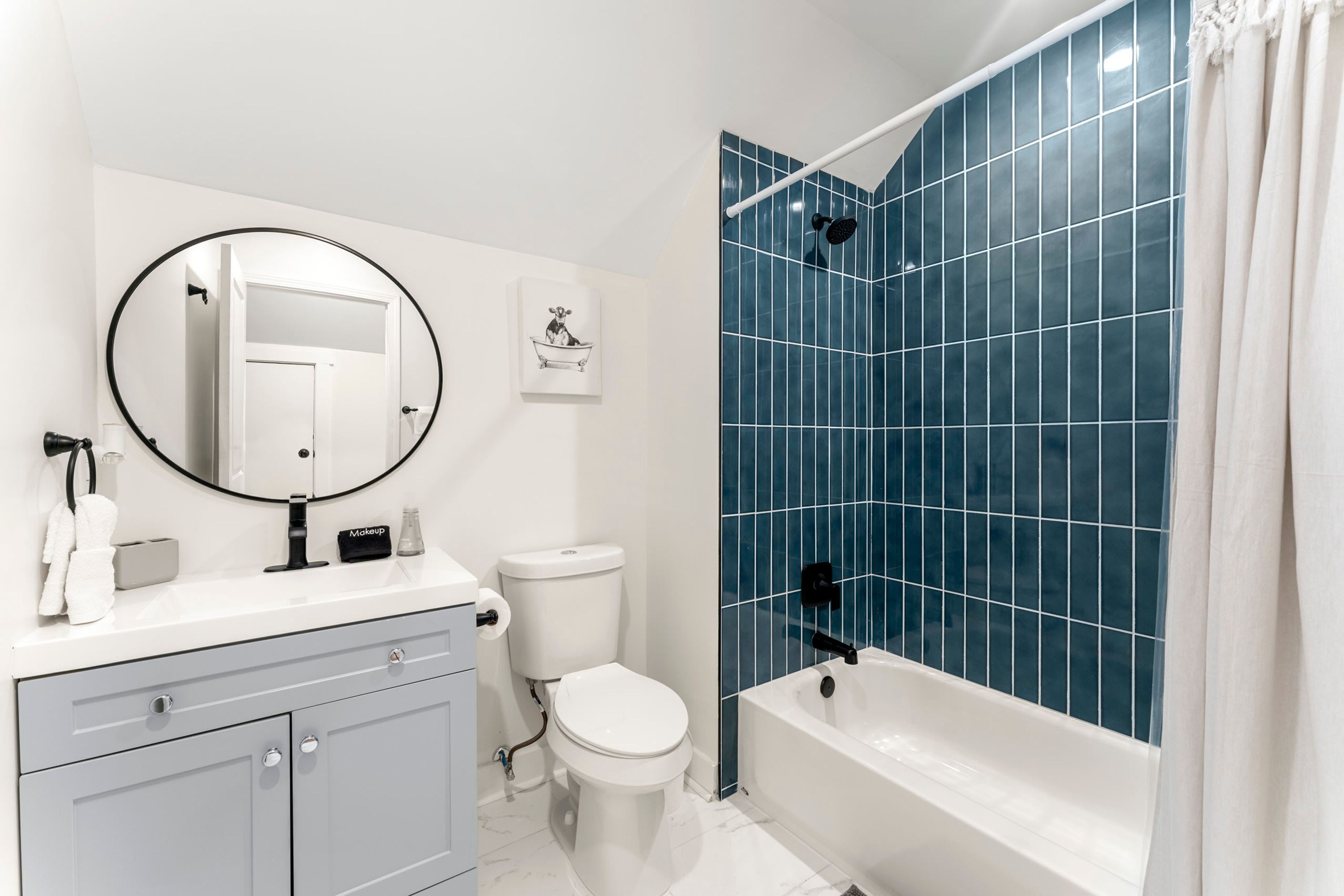 A bathroom with a white vanity, a toilet, a bathtub with blue tiles, and a shower area.