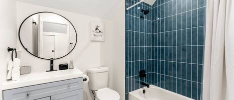 A bathroom with a white vanity, a toilet, a bathtub with blue tiles, and a shower area.