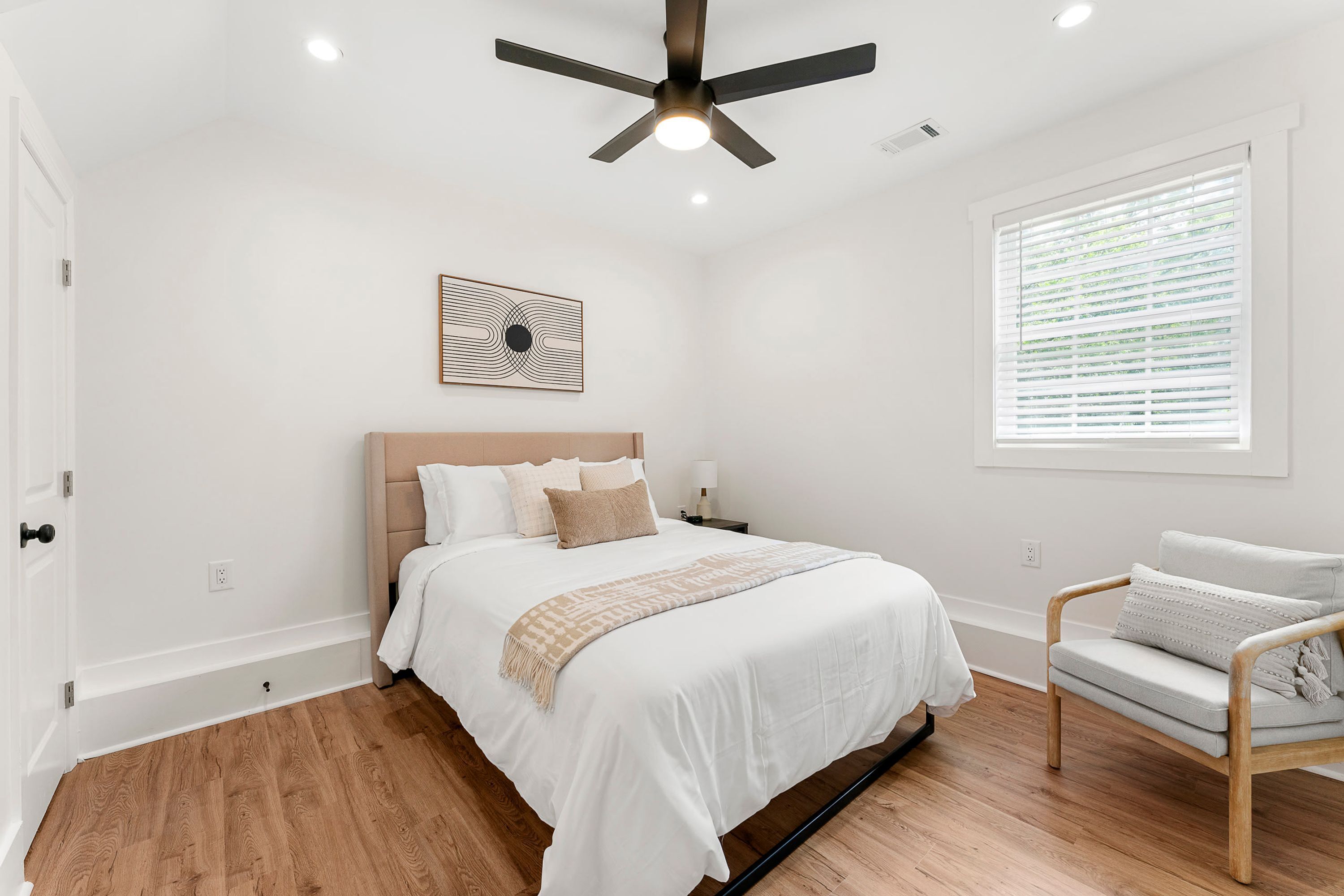 A bedroom with a bed, a ceiling fan, a window with blinds, and a chair.