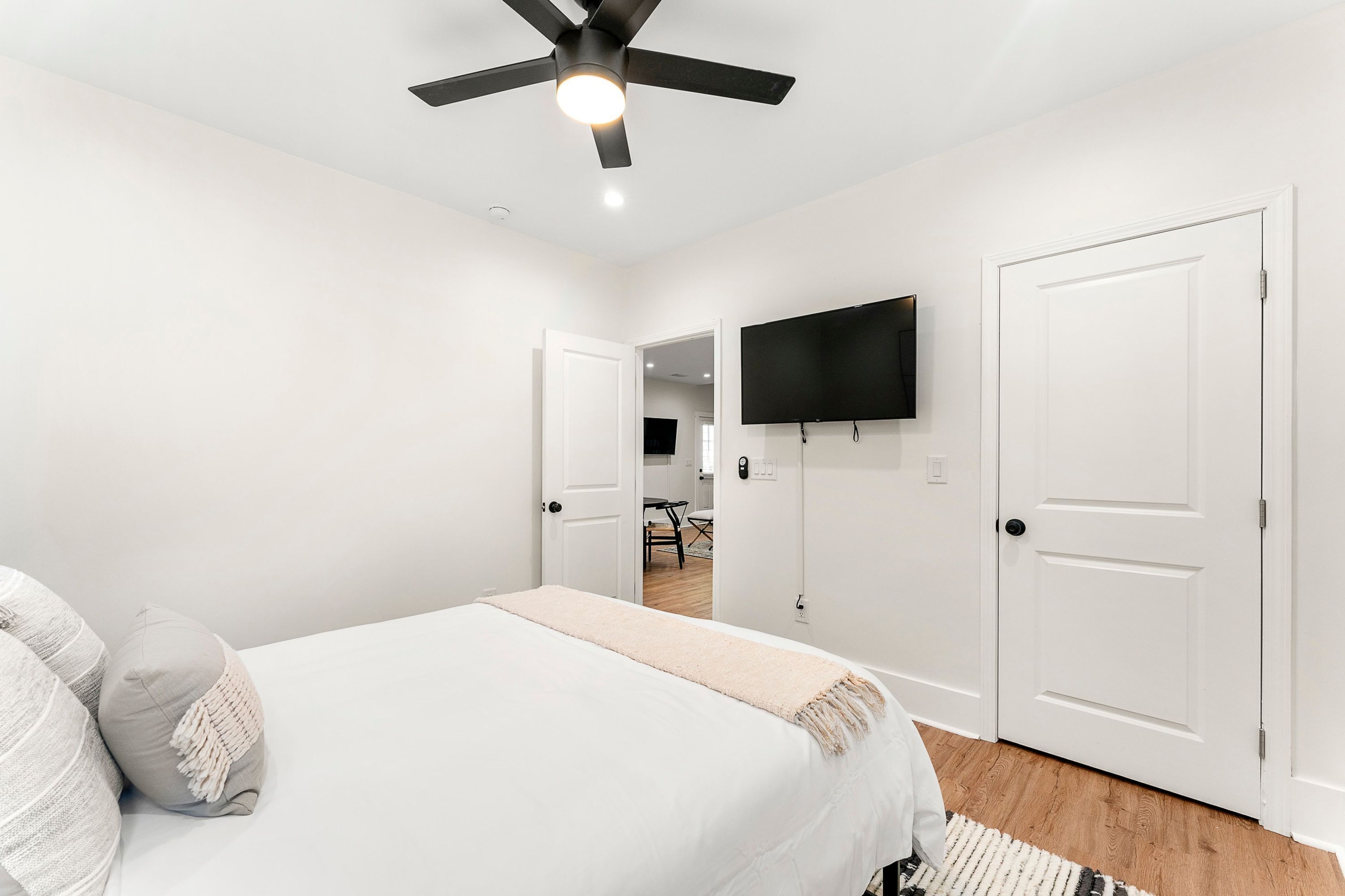 Un dormitorio con cama, ventilador de techo, televisor montado en la pared y puertas blancas.