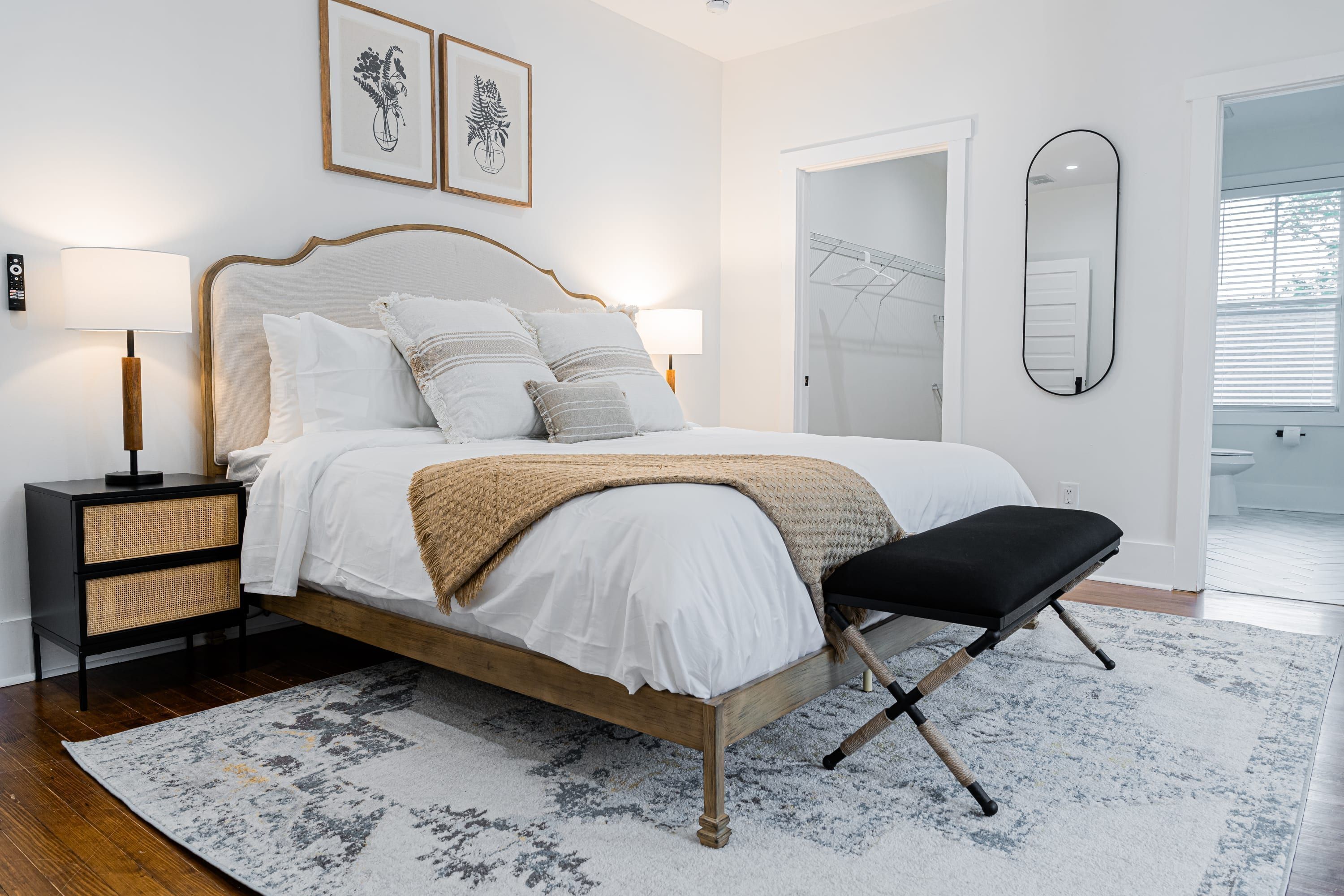 A neatly arranged bedroom with a bed, bedside tables, a bench, and a large mirror.