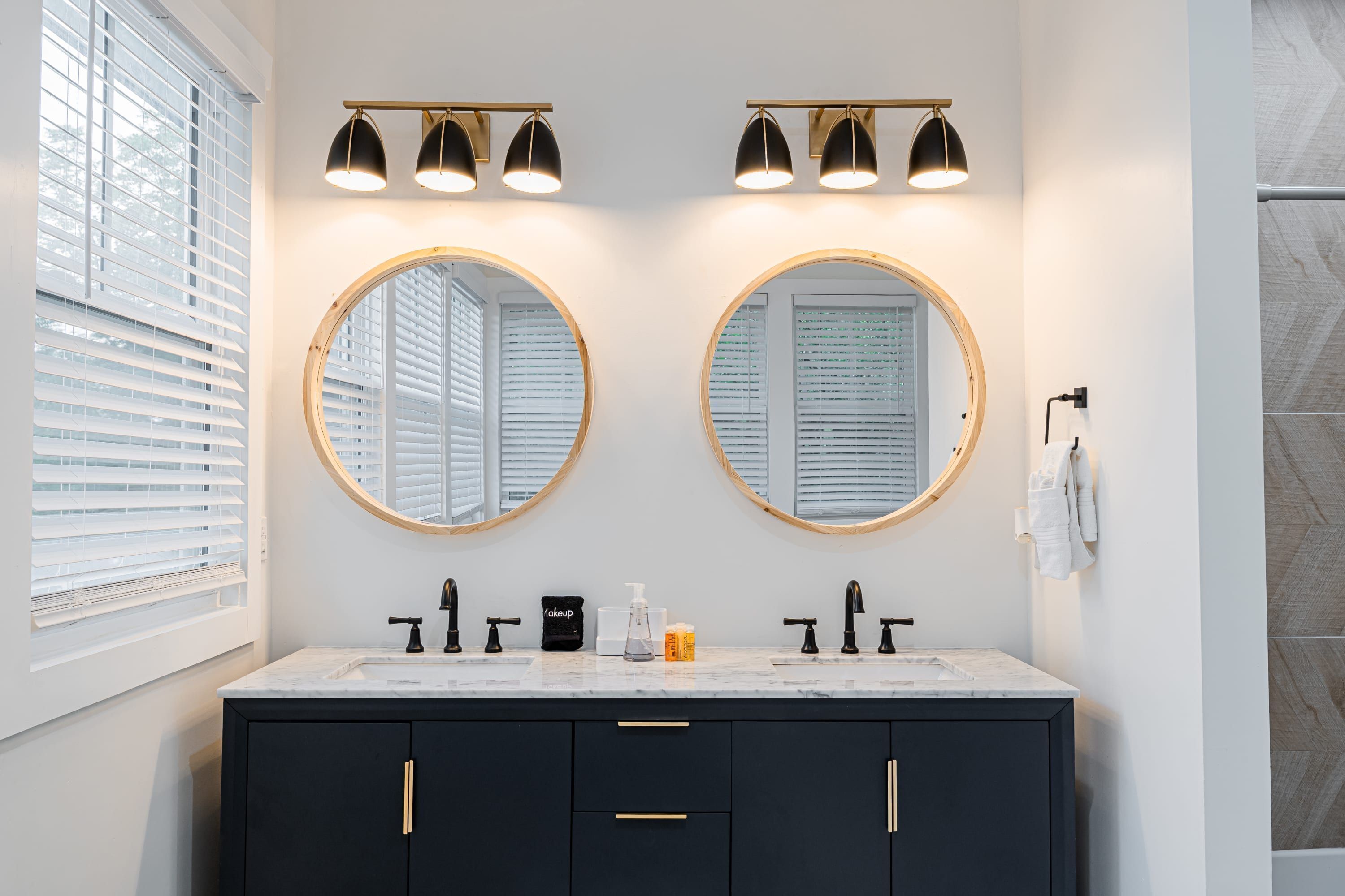 Un bagno con due specchi rotondi, rubinetti neri e un piano di lavoro bianco.