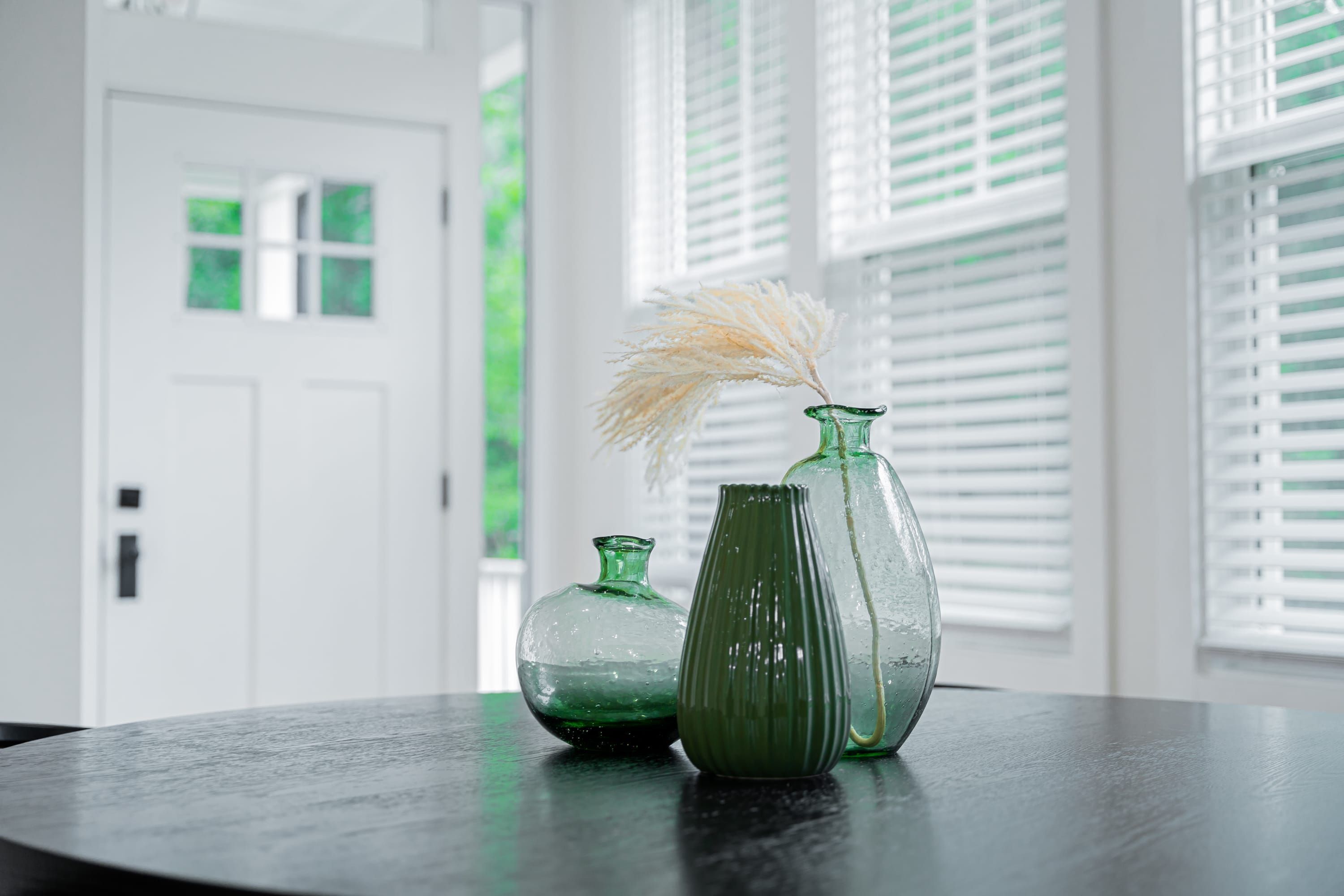 Three glass vases on a dark surface with a white door and windows in the background.