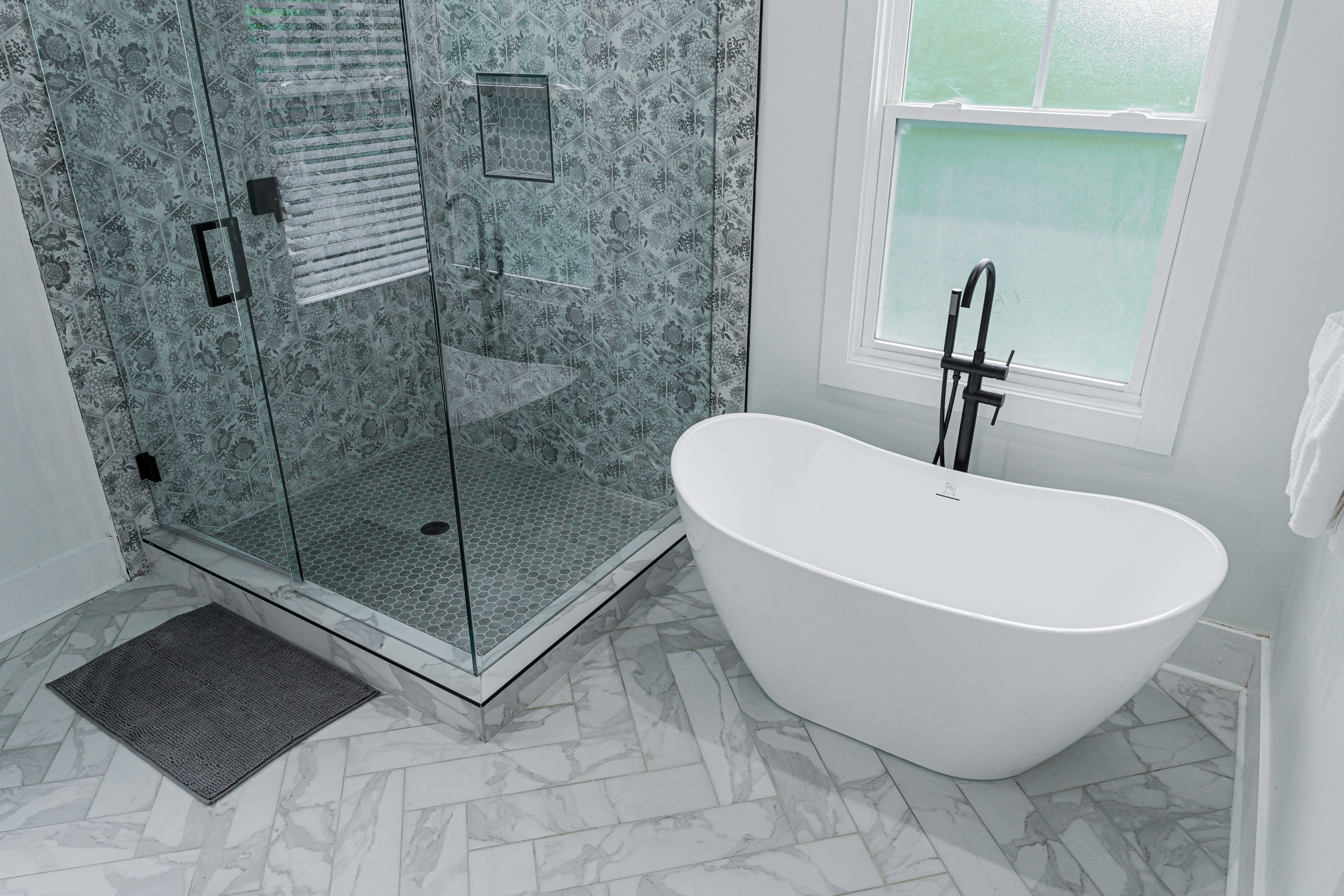 A modern bathroom with a freestanding bathtub, a glass-enclosed shower, and a large window providing natural light.
