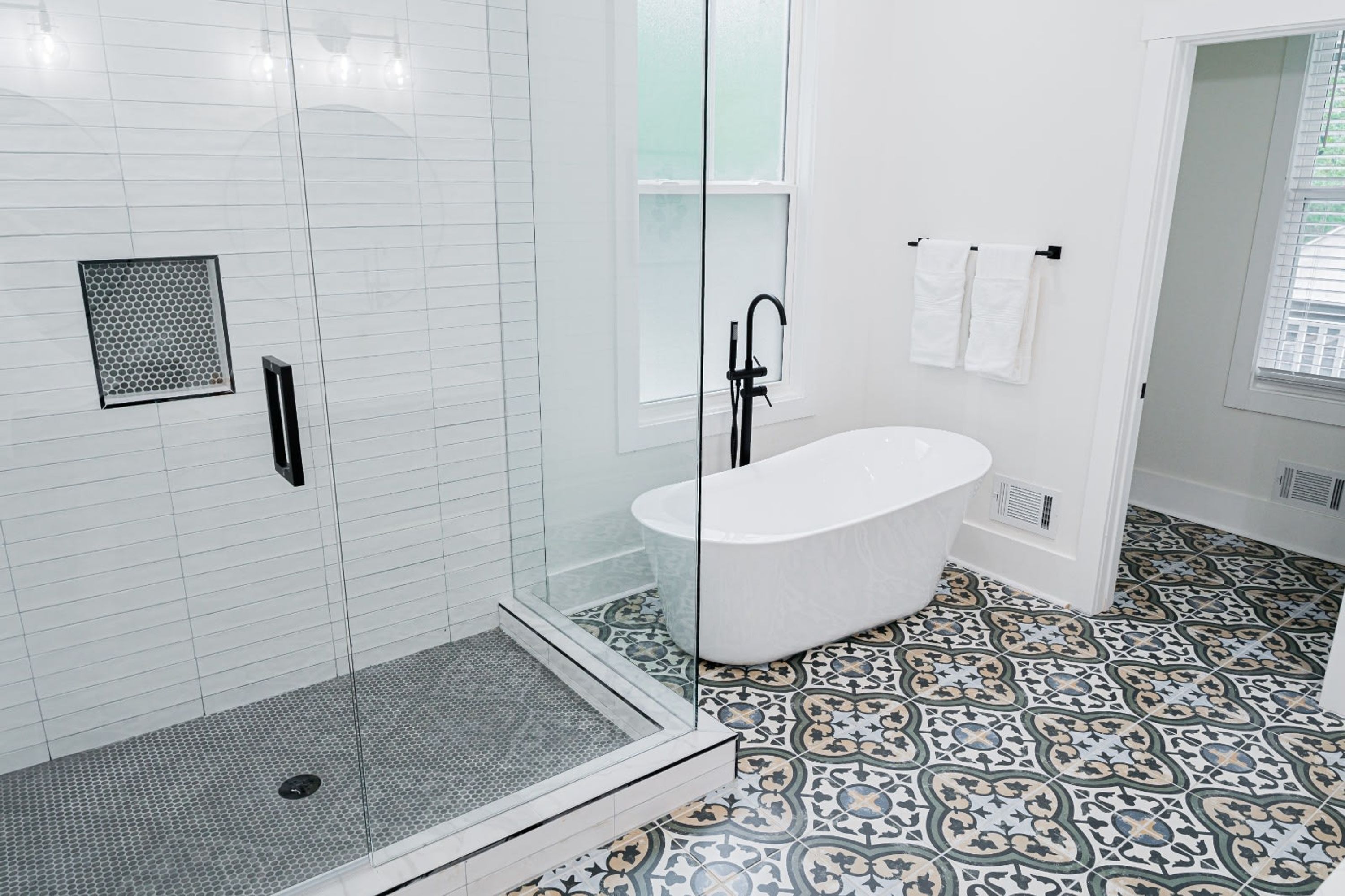 Un baño moderno con ducha de vidrio, bañera independiente y baldosas de piso estampadas.
