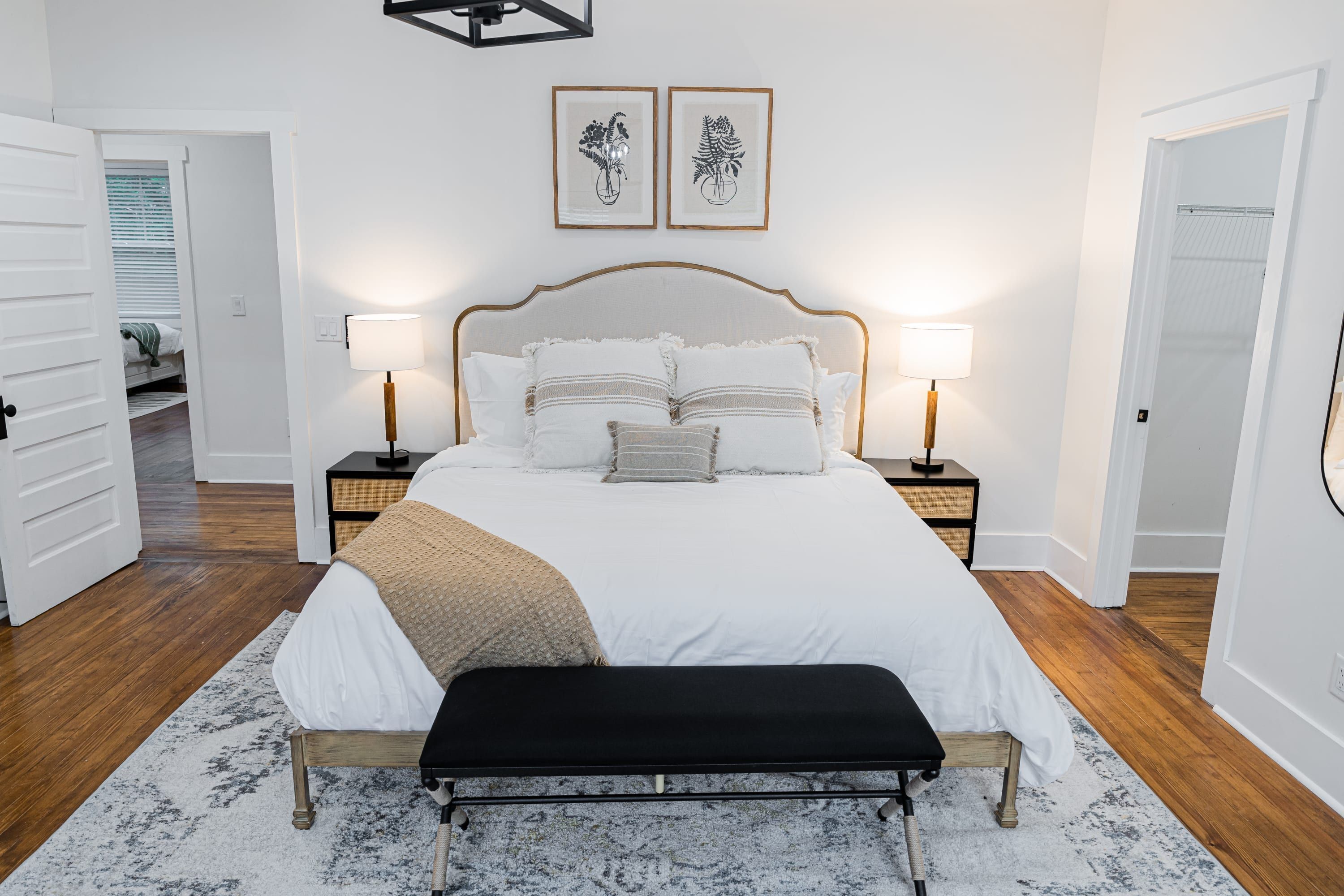 A bedroom with a large bed, bedside lamps, a bench, and two framed pictures on the wall.