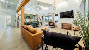 A modern living room with a sofa, a black chair, a TV, and a kitchen in the background. - Brycegate Retreat, Cabin, Star Dome Bedroom, Fire Pit, Hammocks, Views, Pets, EV (Hatch)