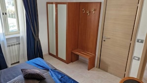 Un dormitorio con cama, un armario con espejos, una banca y una ventana con cortinas.