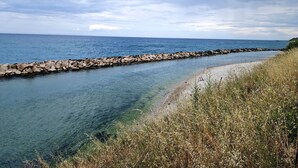 Escena costera con una vista despejada del mar, un rompeolas rocoso y una zona cubierta de hierba.