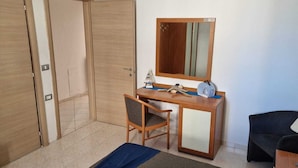 Una habitación con un escritorio de madera, una silla, una mesita, un espejo y un sofá.
