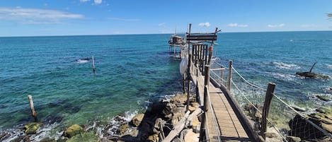 Un muelle de madera que se adentra en un mar azul cristalino con una costa rocosa.