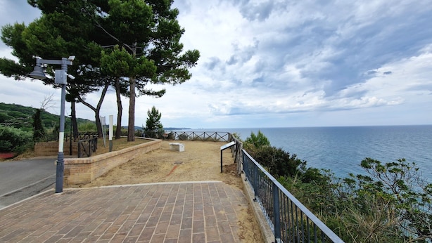 Un camino pavimentado con barandilla de metal que conduce a una playa, con vistas al mar.