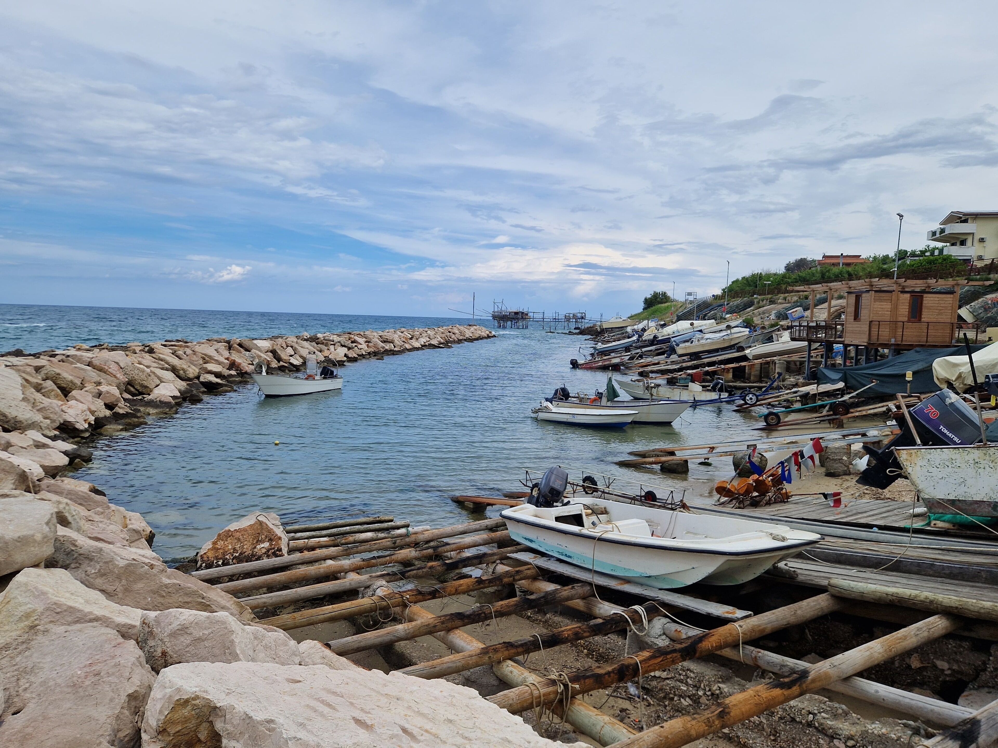 Escena costera con barcos amarrados a un muelle, rodeada por rompeolas rocosas y una estructura de madera.