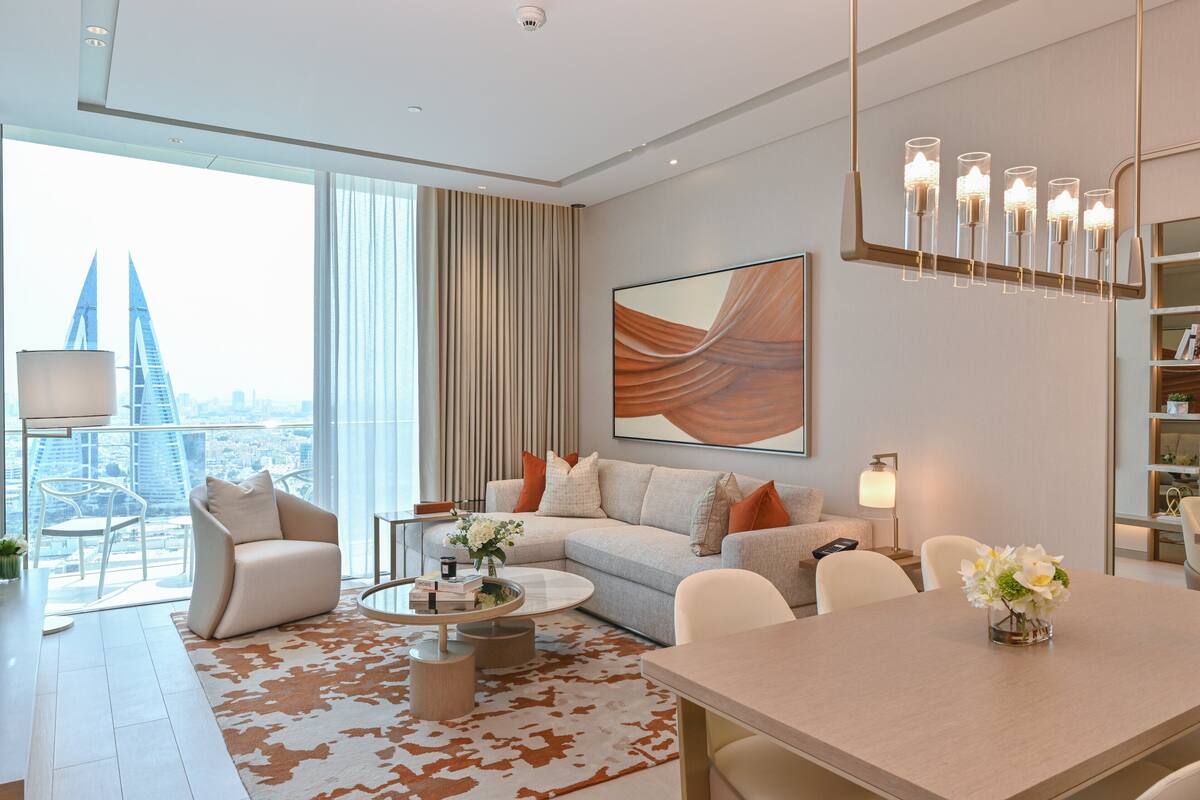 A modern living room with a sofa, coffee table, and a dining table with a vase of flowers.