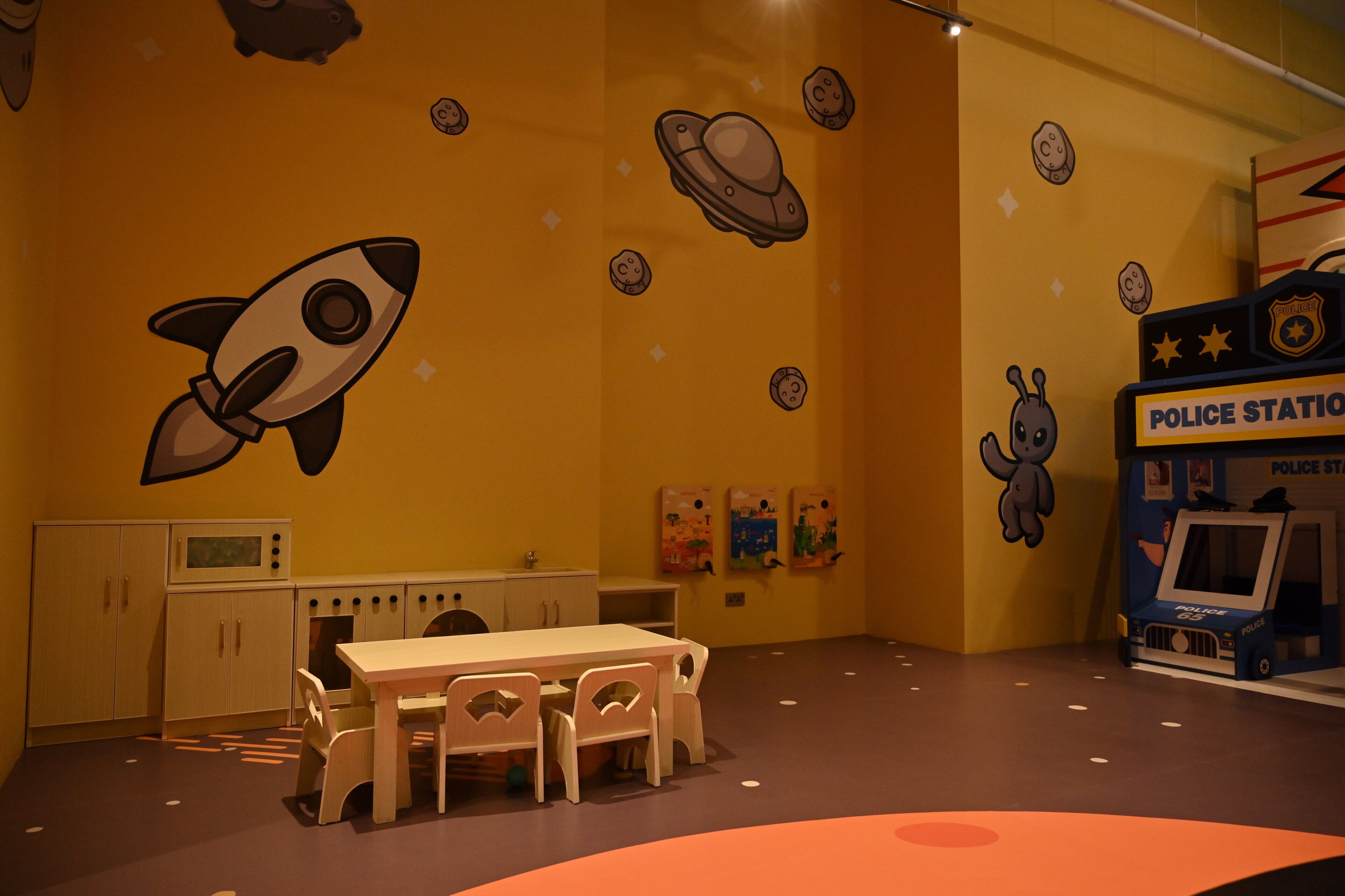 A playroom with a rocket, police station playset, and a table with chairs.
