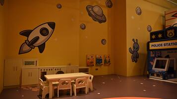A playroom with a rocket, police station playset, and a table with chairs.