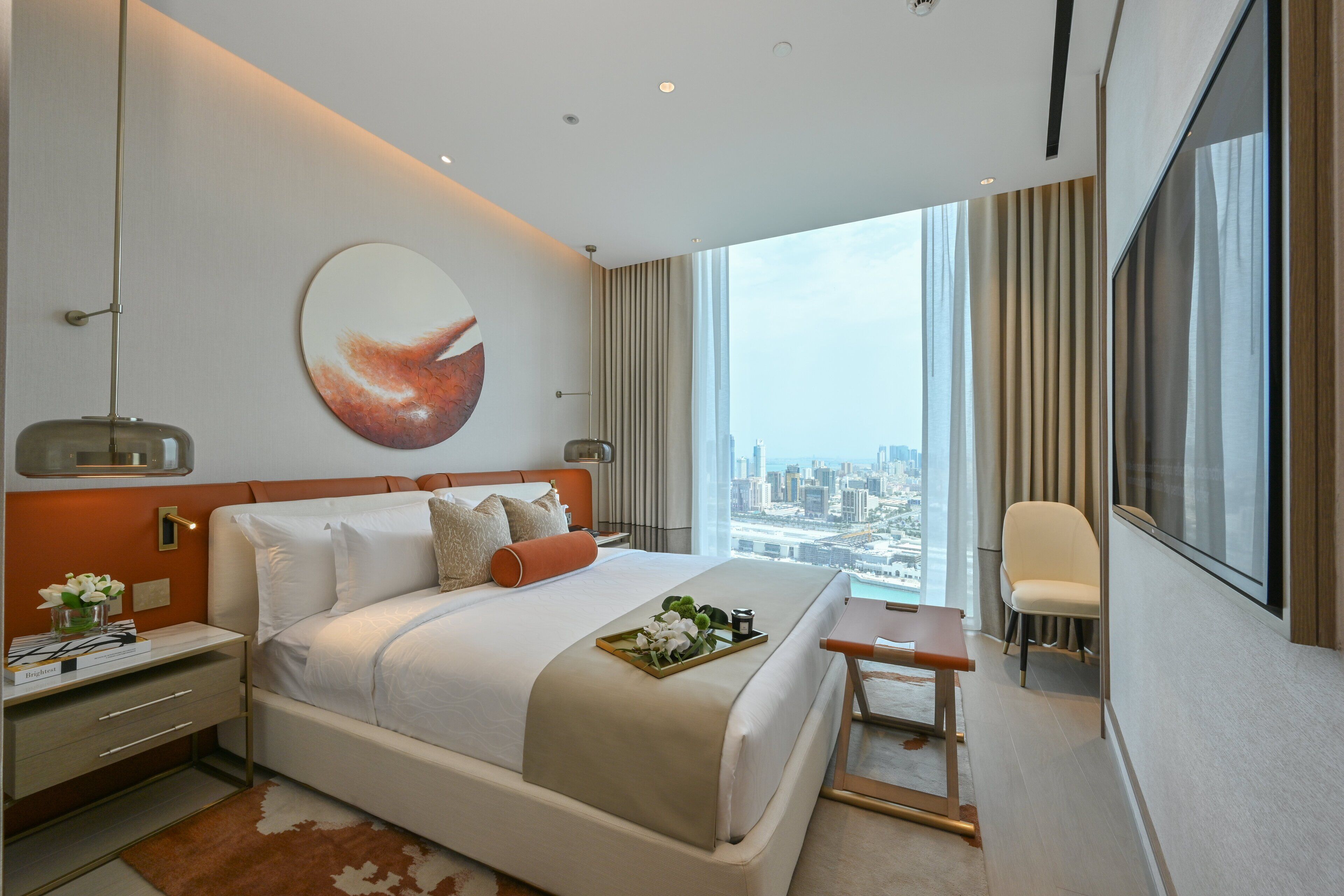 A modern hotel room with a large bed, a city view, a small table, and a chair.