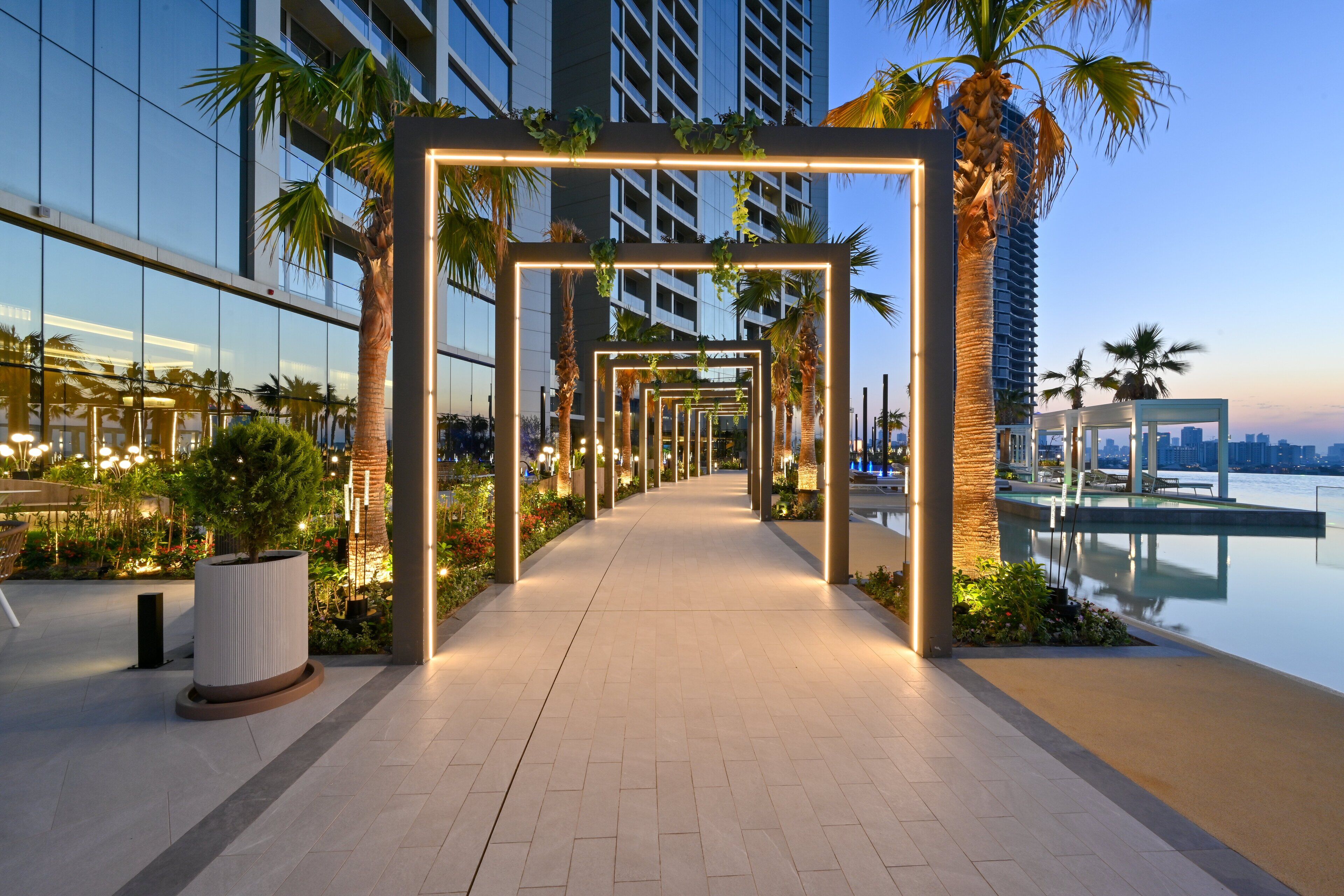 A modern outdoor corridor with a glass building on one side and a pool area on the other.