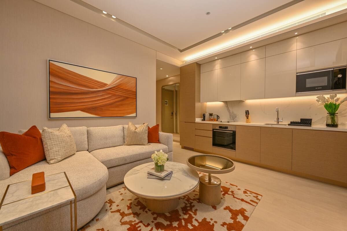 A modern living room with a sectional sofa, a coffee table with a book and flowers, and a kitchen with built-in appliances.