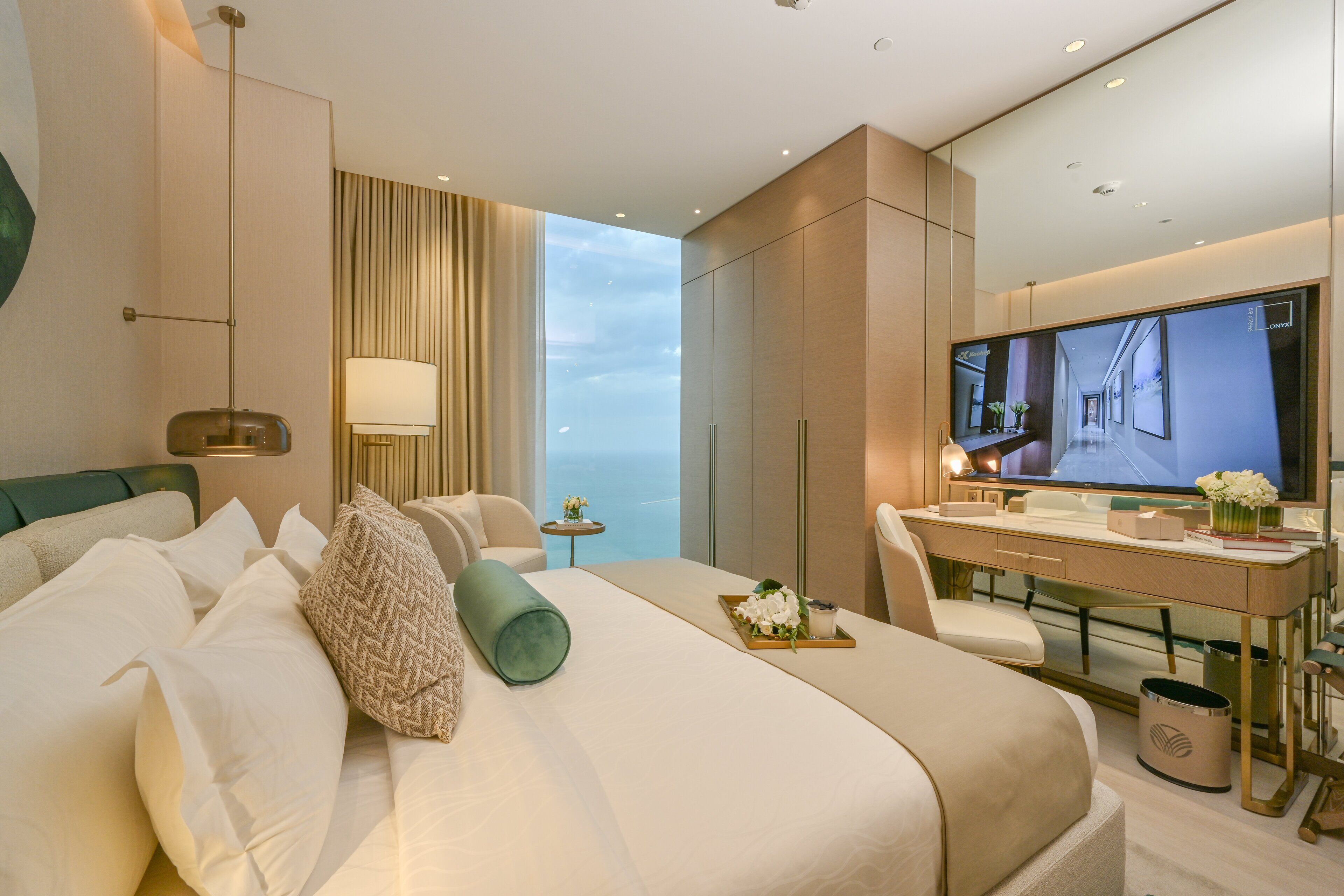A modern hotel room with a large bed, a desk, a TV, and a view of the sky.