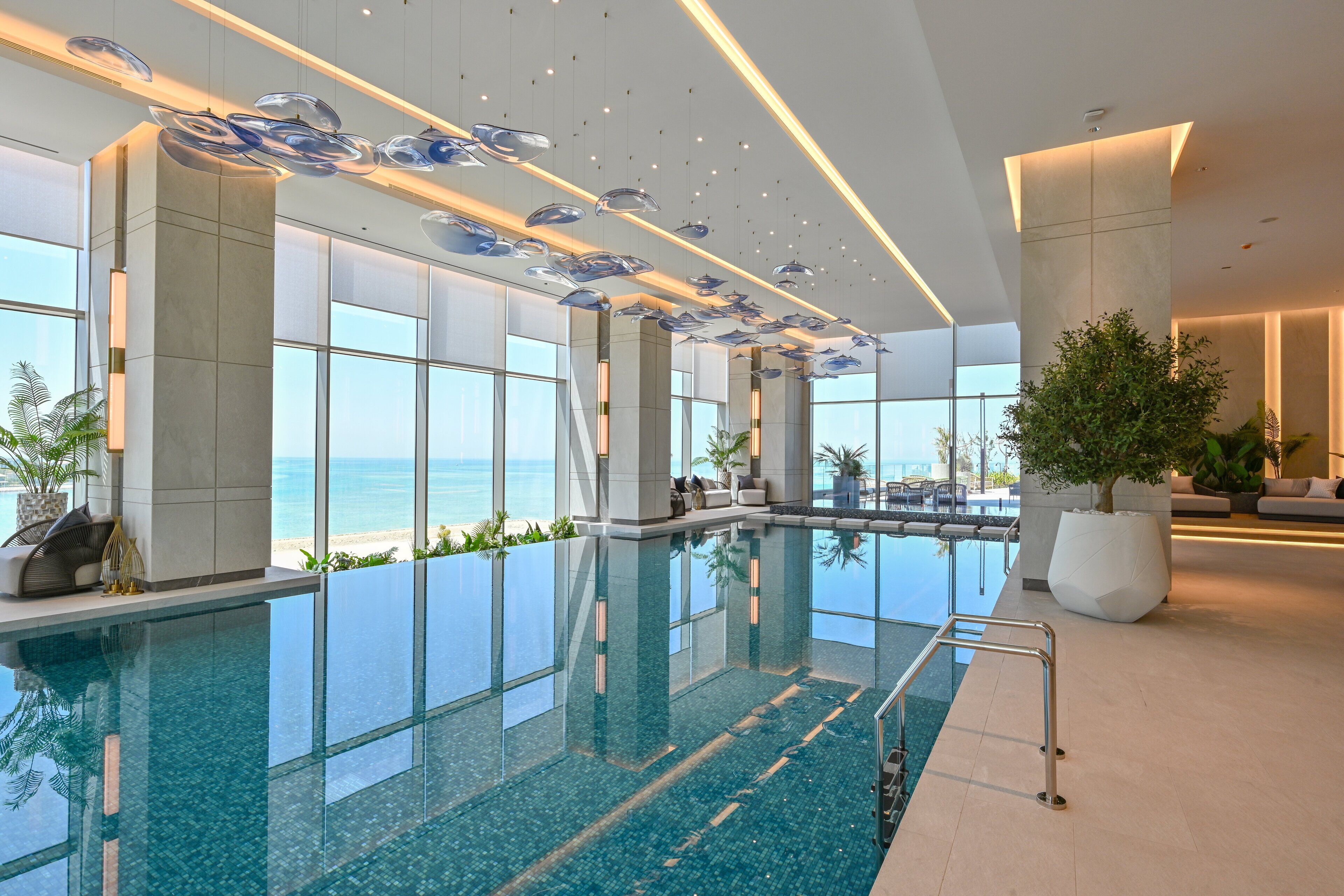 Una piscina interior moderna con paredes de vidrio transparente, ventanas amplias y vistas al océano.