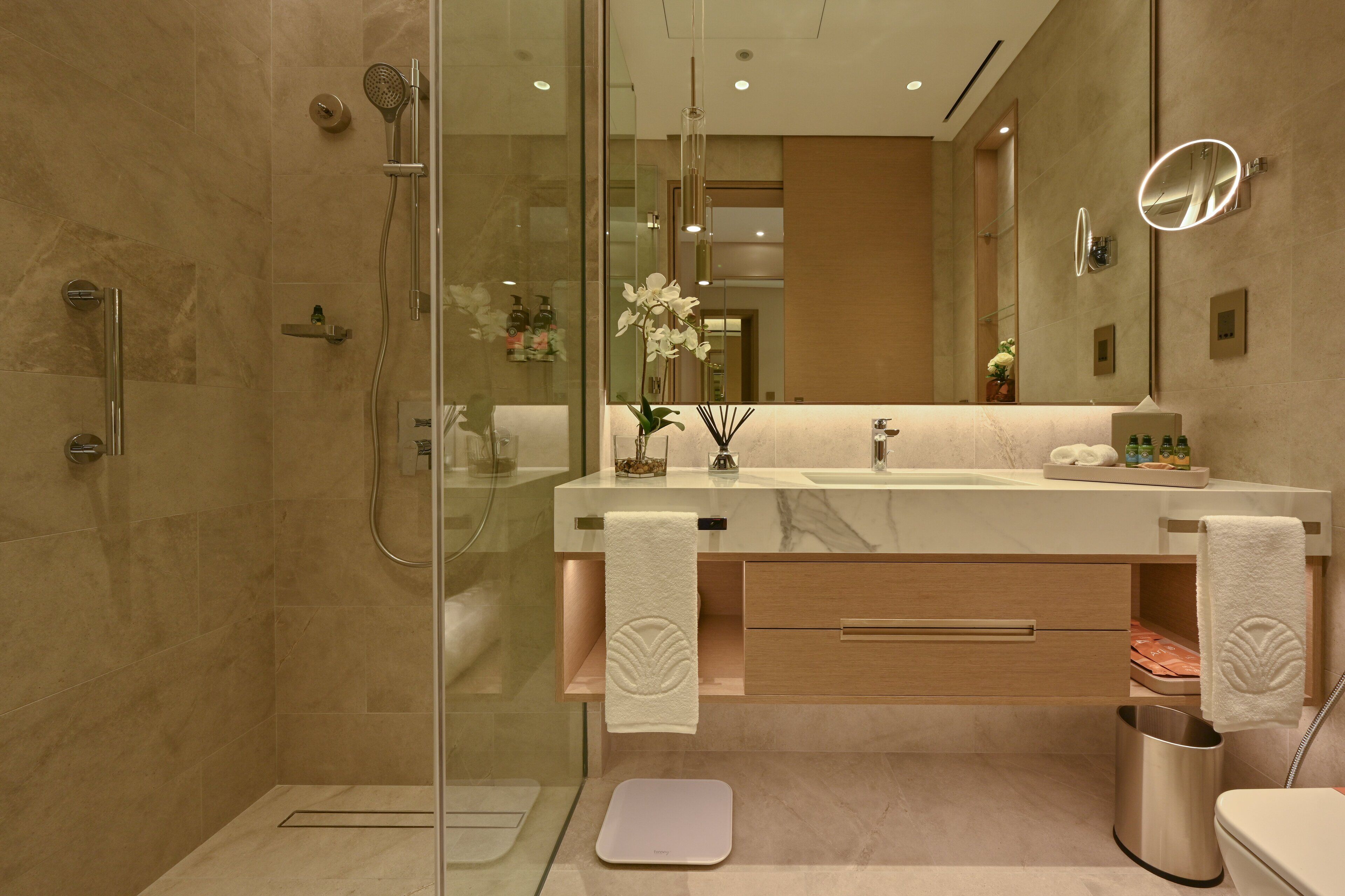 Une salle de bain moderne avec une douche à parois de verre, un lavabo en marbre et un grand miroir.