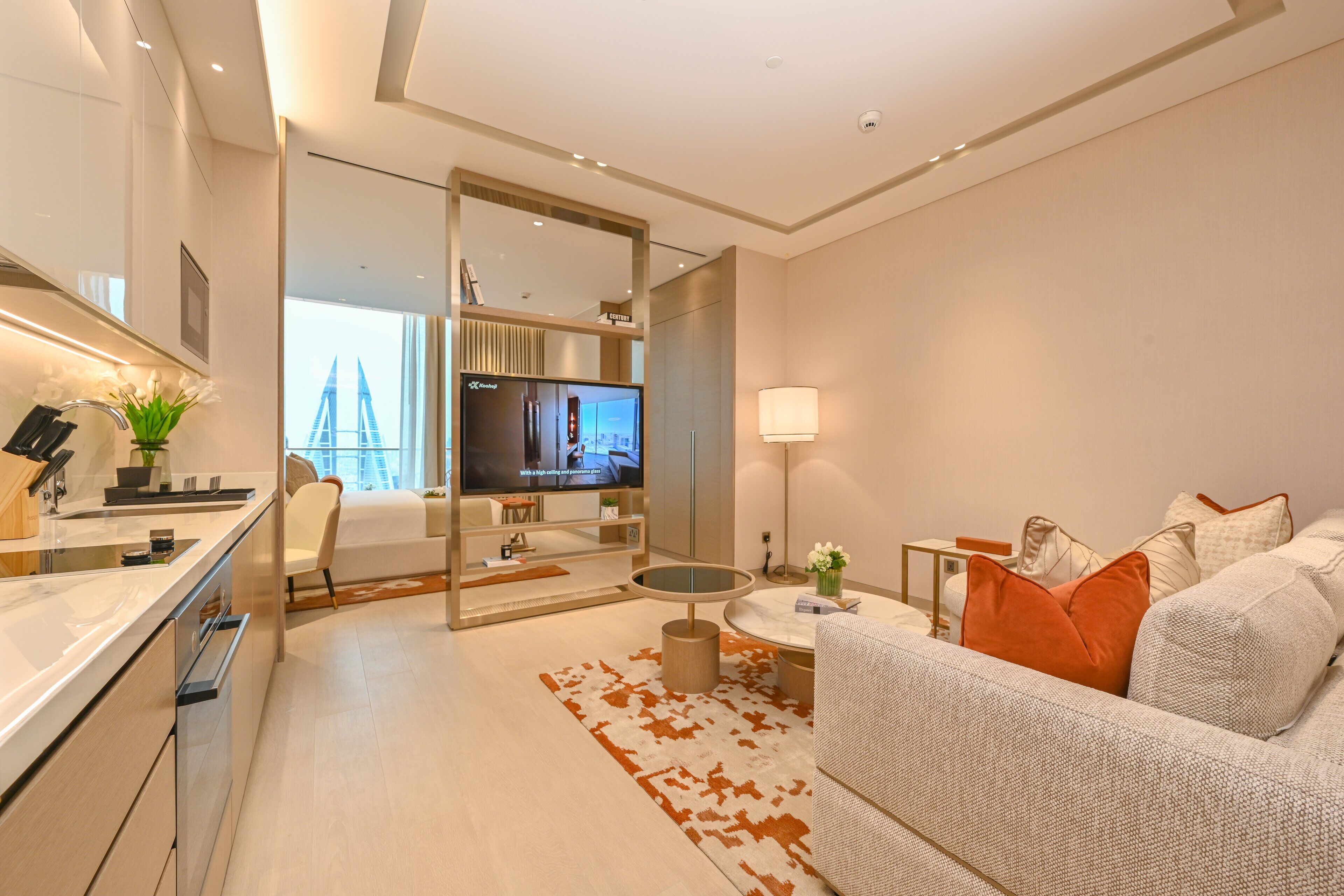 Une chambre d’hôtel moderne dotée d’un coin cuisine, d’un salon avec un canapé et une télévision, ainsi que d’une grande fenêtre offrant une vue sur la ville.