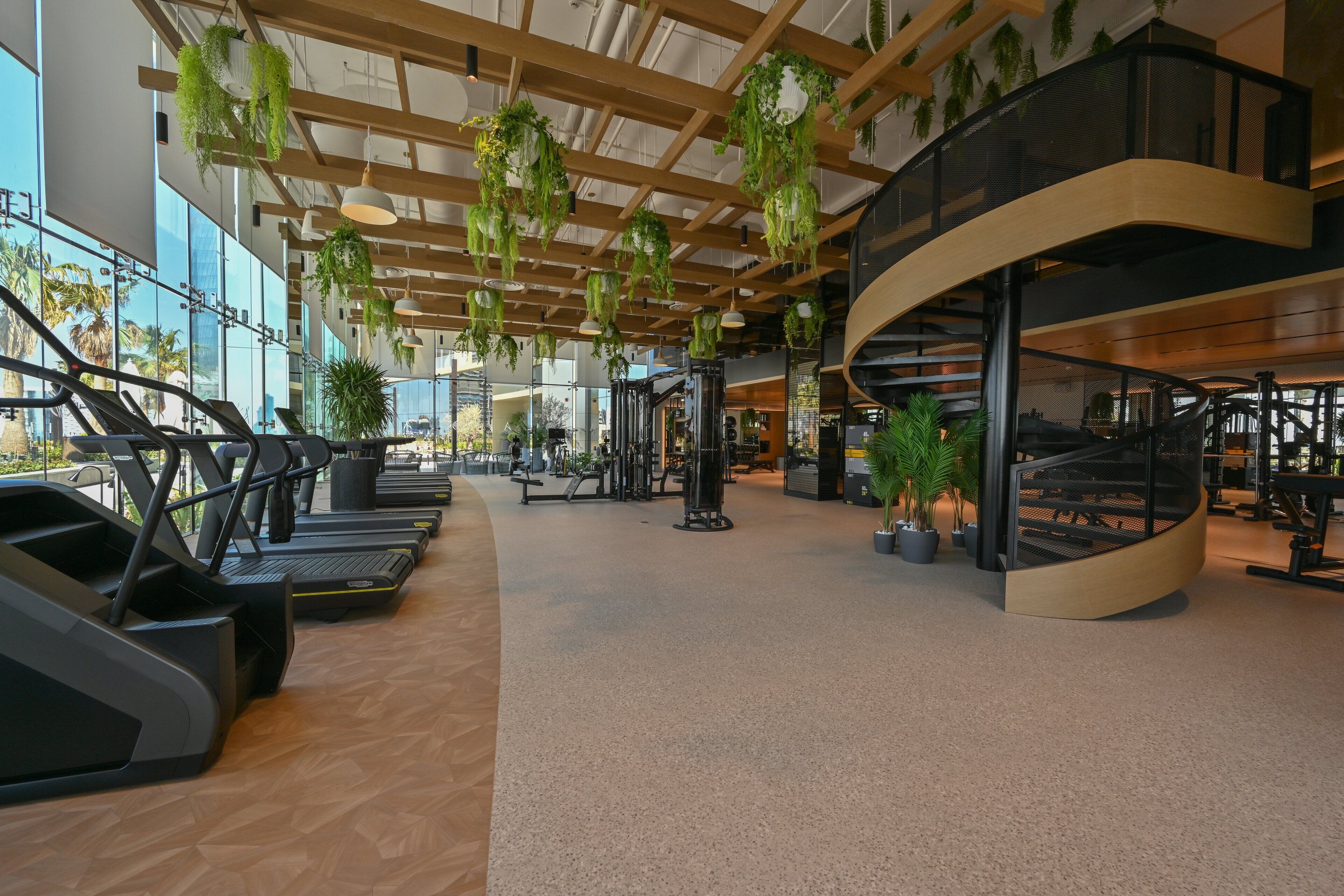 A spacious gym with treadmills, exercise equipment, and a curved staircase.