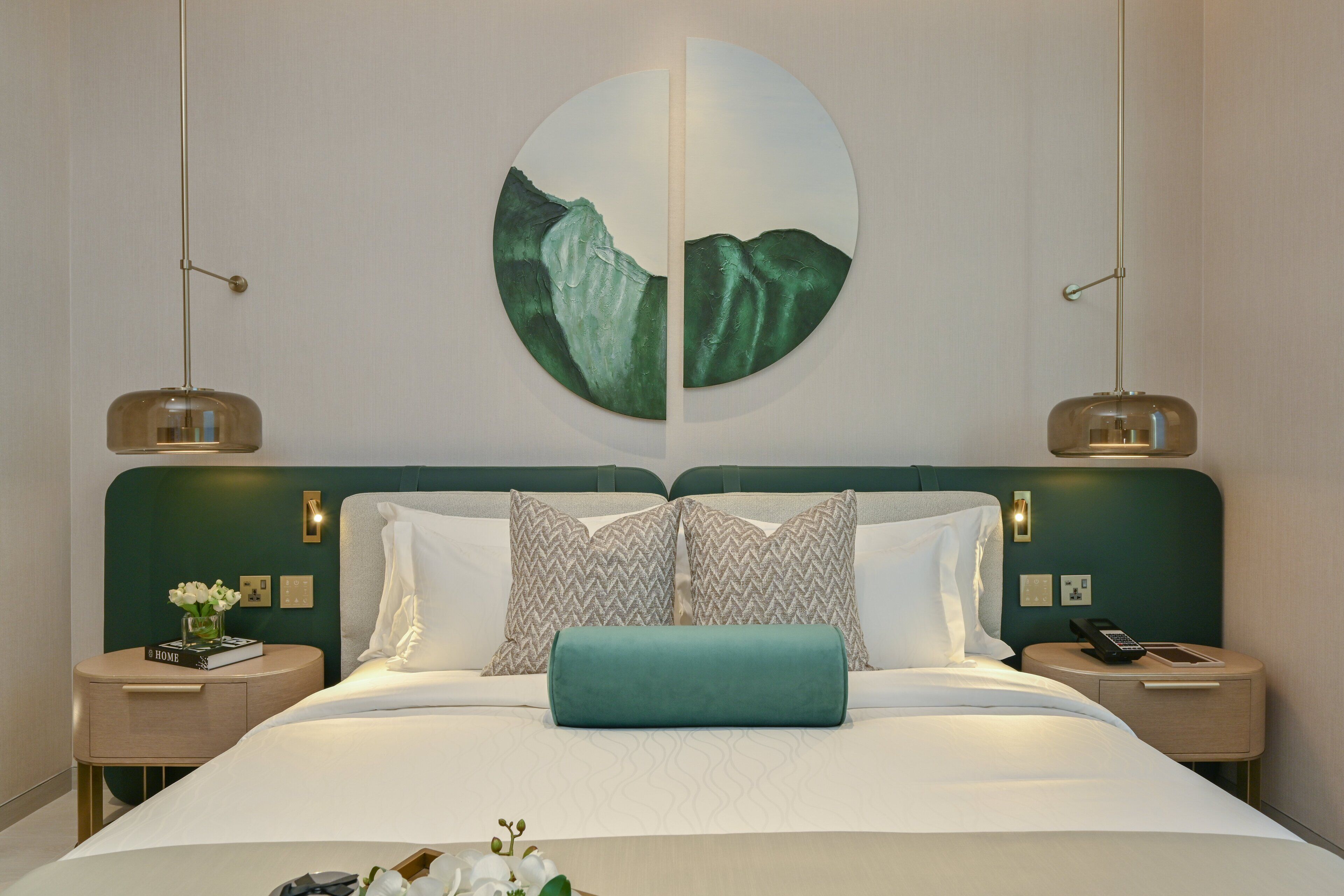 A modern hotel room with a large bed, two bedside tables, and a wall-mounted artwork.