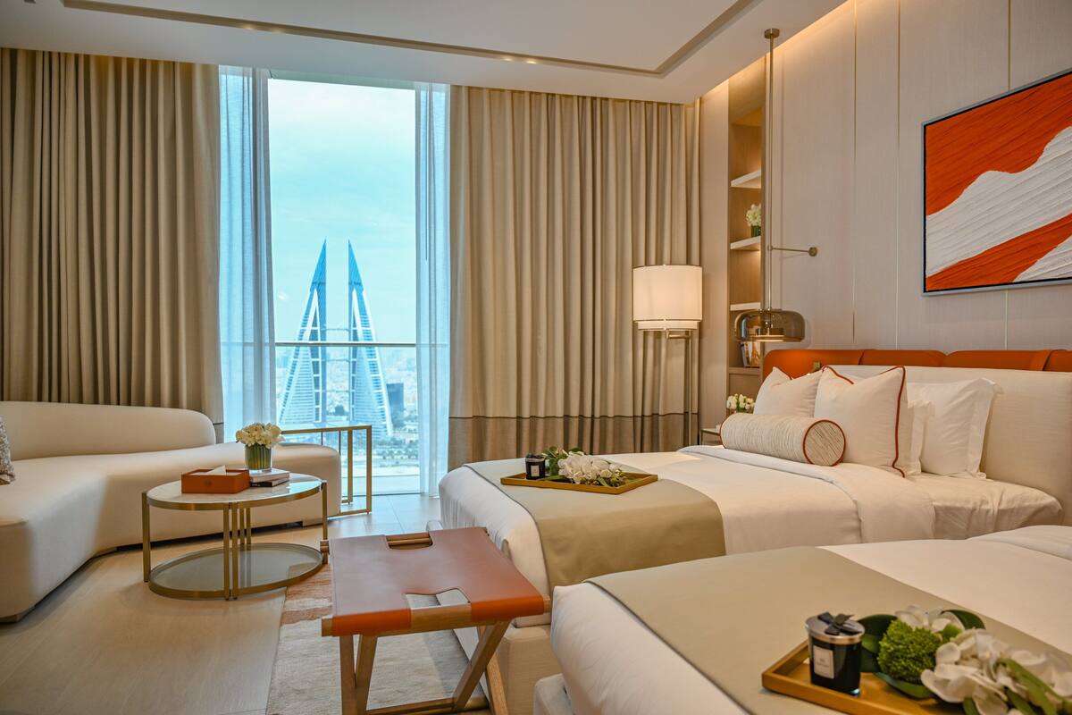 A hotel room with a large bed, a smaller bed, a sofa, a round table, and a view of a building through the window.