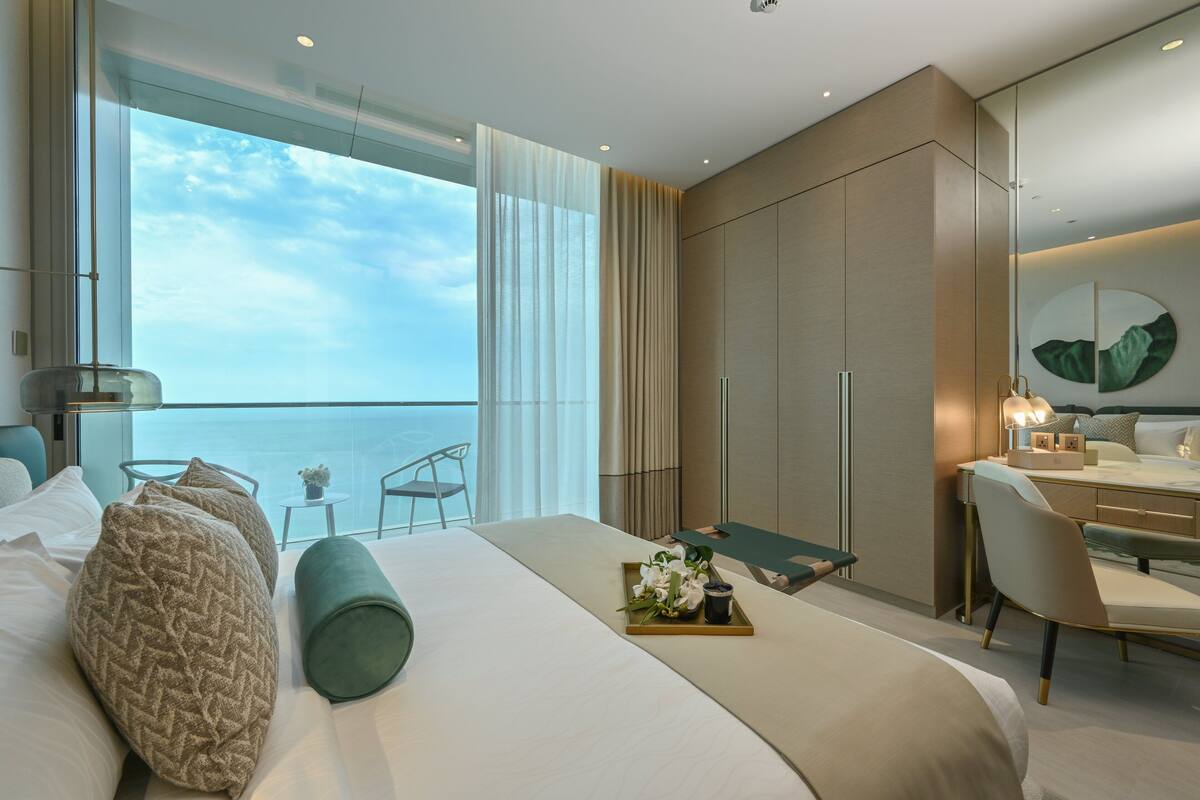 A modern hotel room with a large bed, a desk, and a view of the ocean.